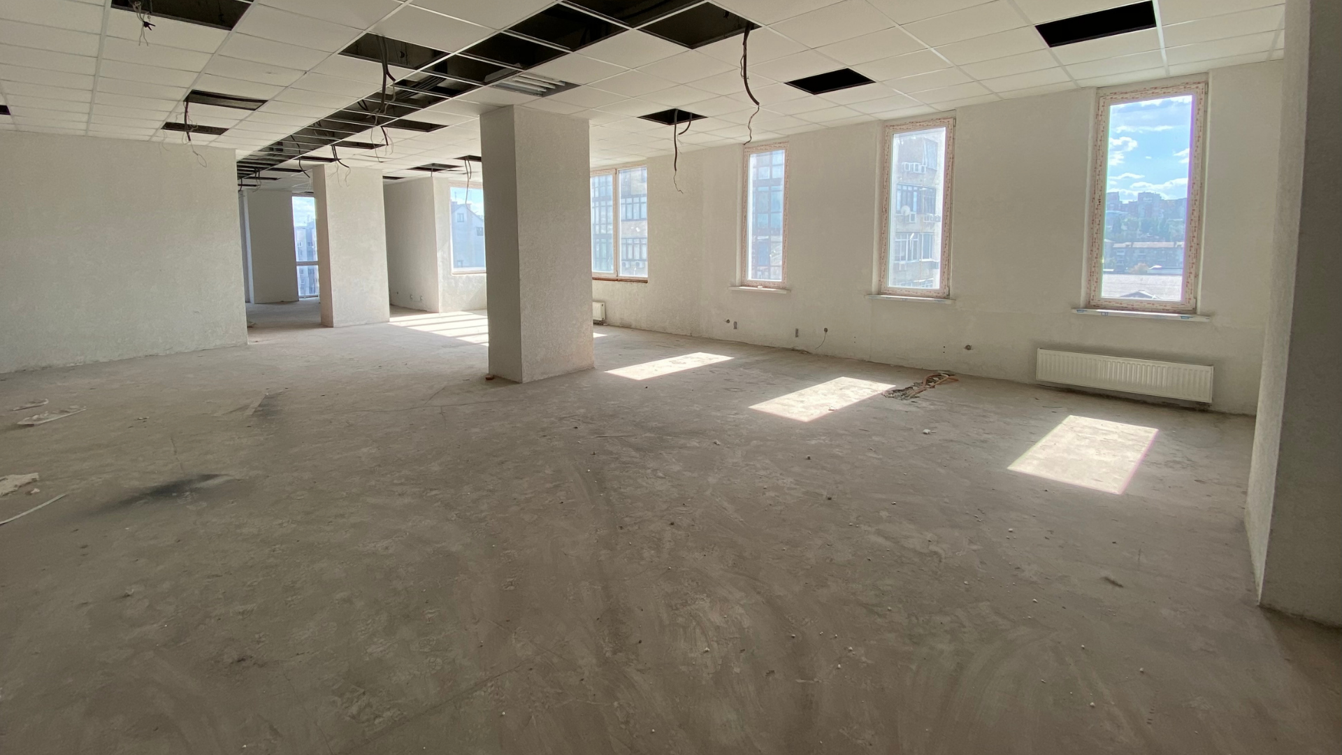 Empty unfinished office interior with white walls, exposed ceiling, and sunlight through tall windows.