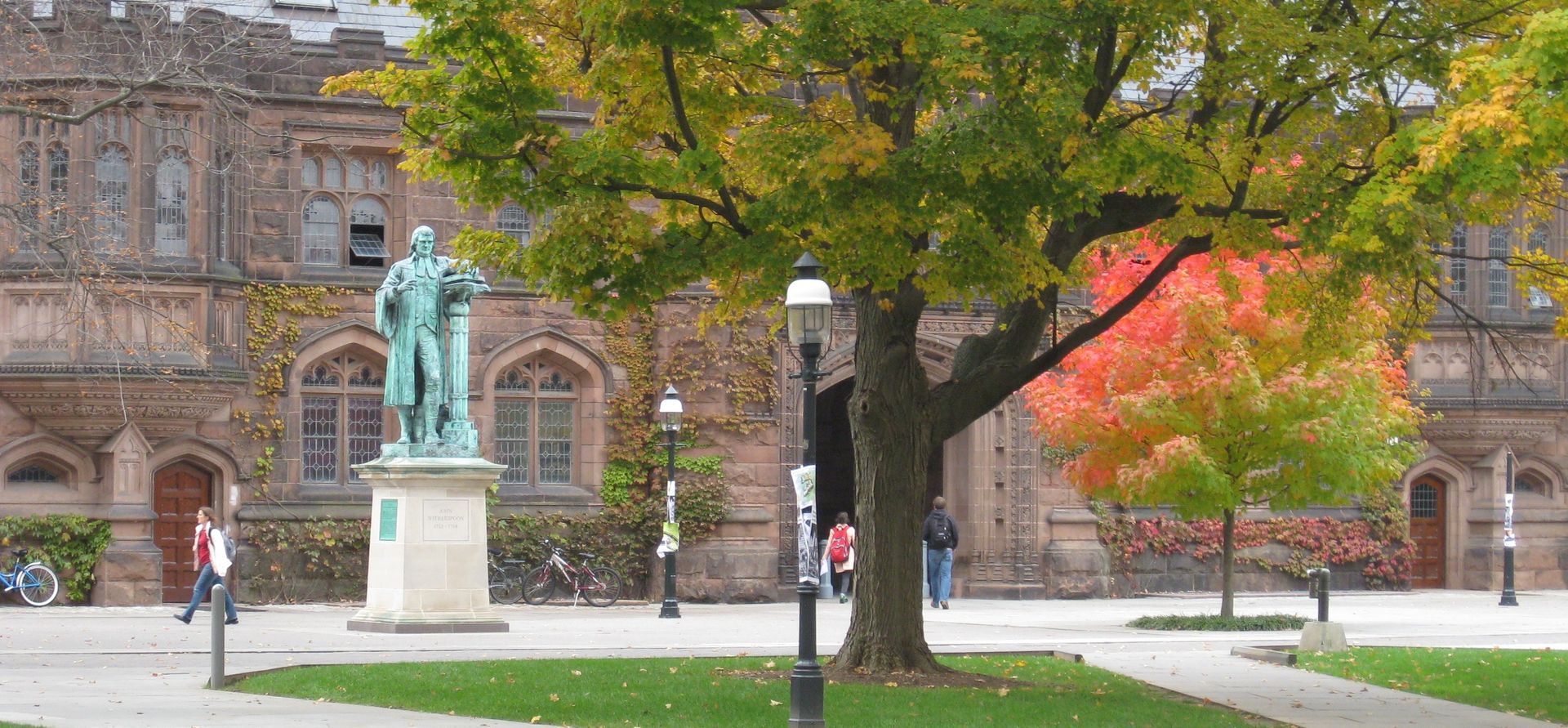 Statue in a campus courtyard with a brick building and trees with green and red autumn leaves