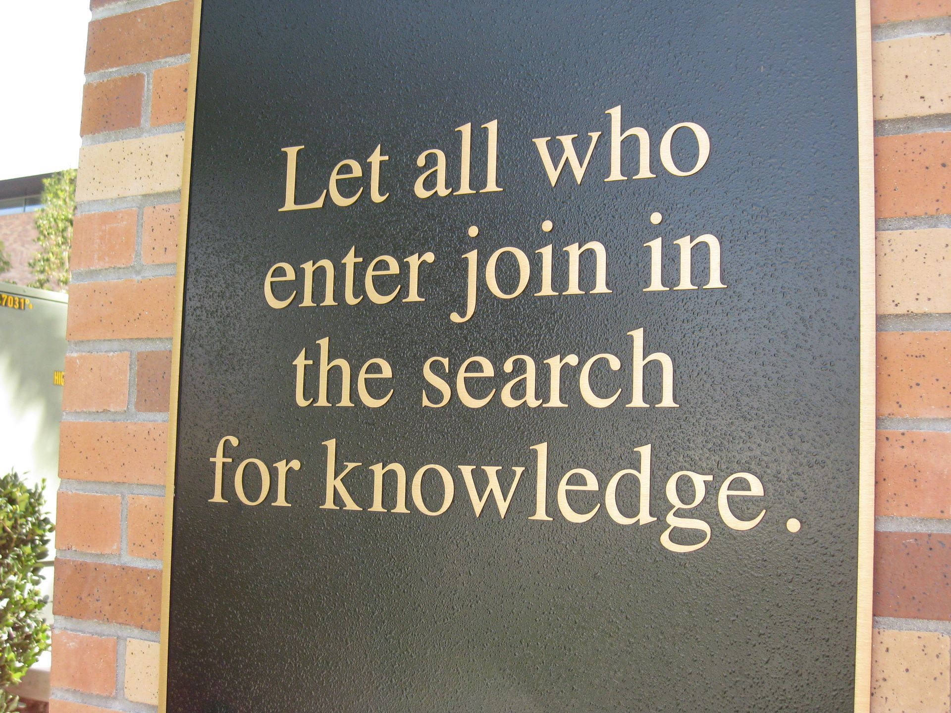 Stone plaque with gold text reading, “Let all who enter join in the search for knowledge.”