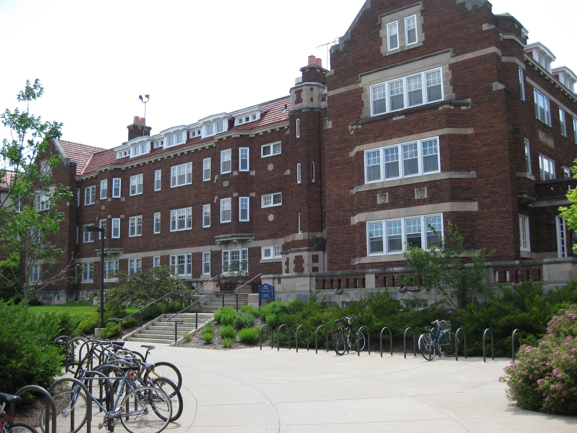 Brick university building with white-trimmed windows, trees, and bicycles parked in front