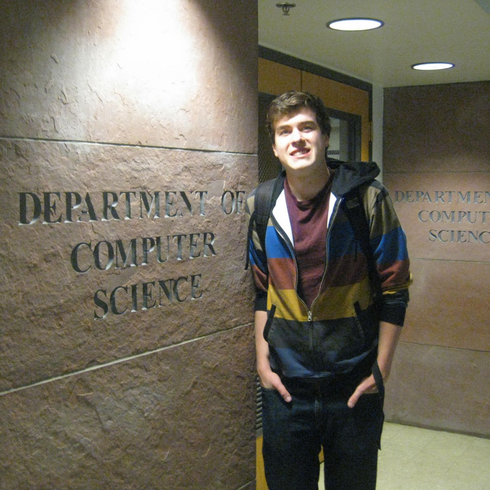 Person standing in a hallway beside a wall sign reading “Department of Computer Science.”