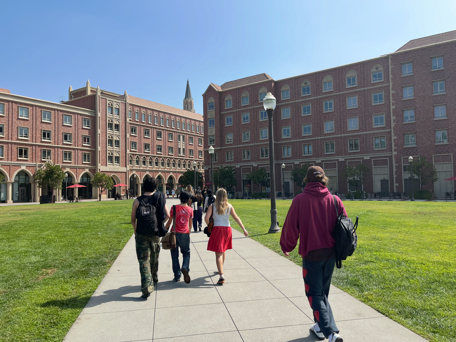 Students walking across a campus lawn between brick academic buildings on a sunny day