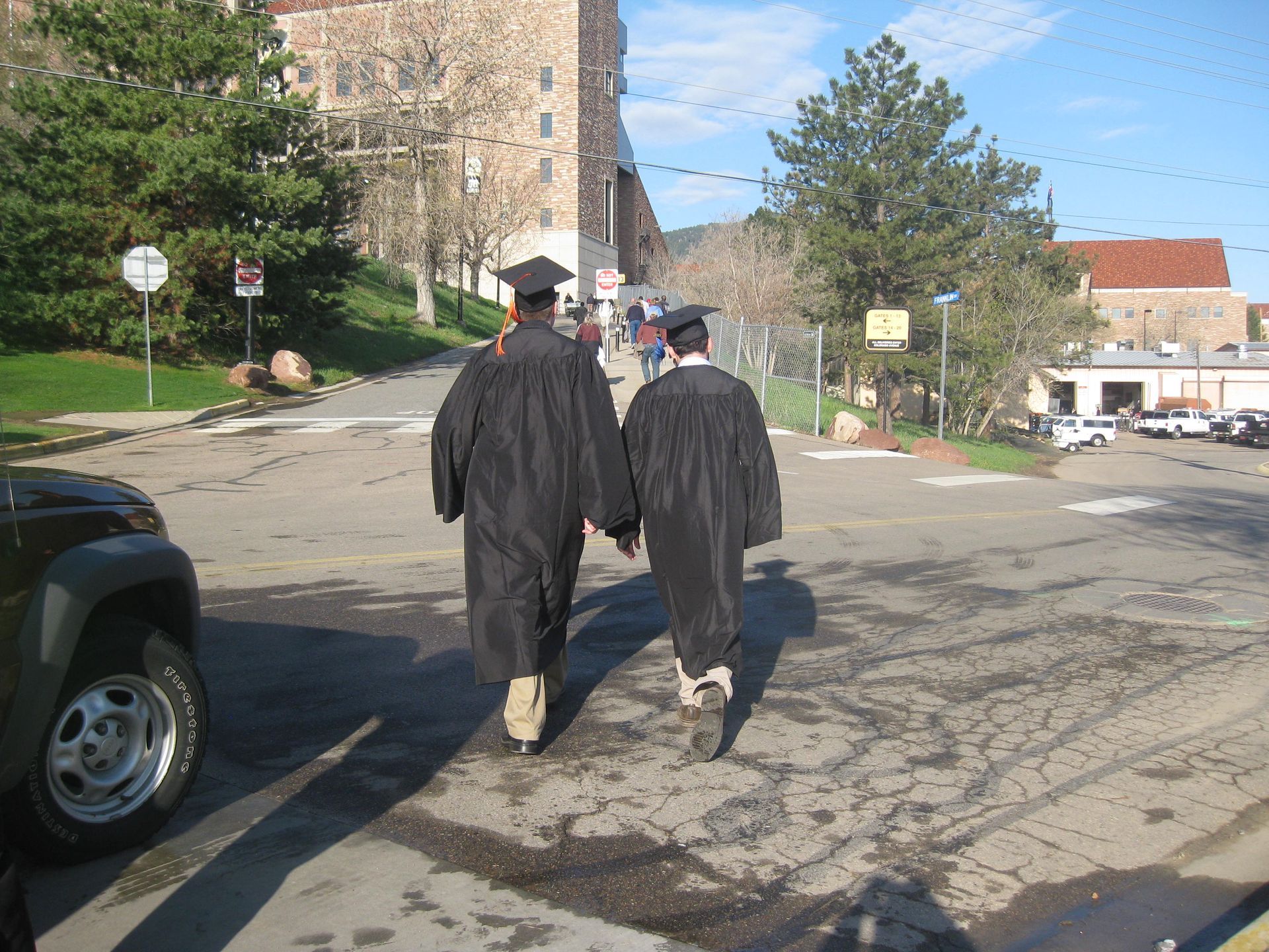 Two graduates in caps and gowns walking down a sunny campus street