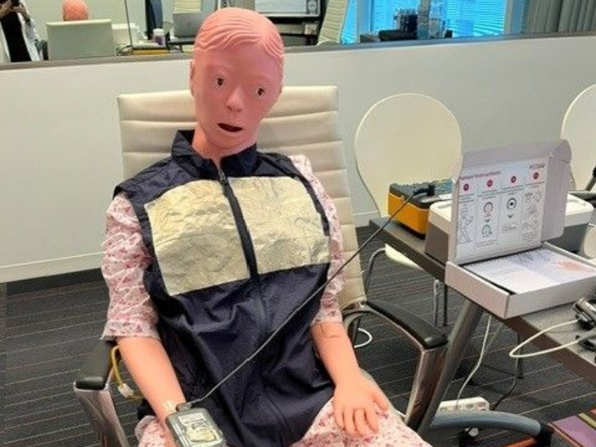Patient manikin dressed and seated for a simulated use testing session with a handheld med
