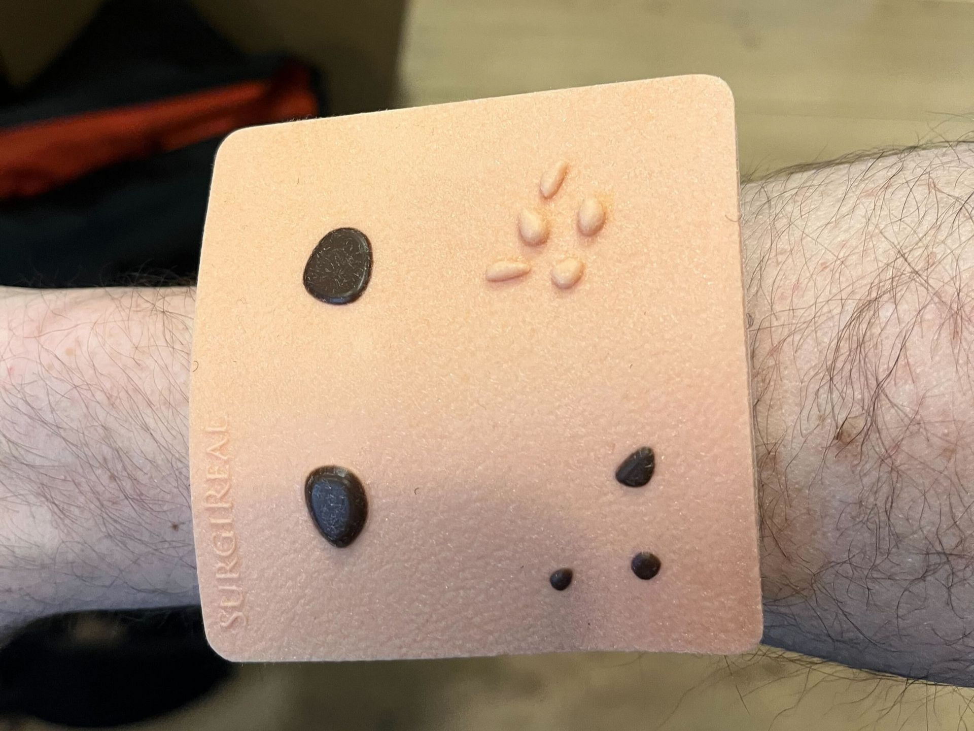 Wearable simulated skin pad with molded moles and skin tags worn on a forearm for device testing