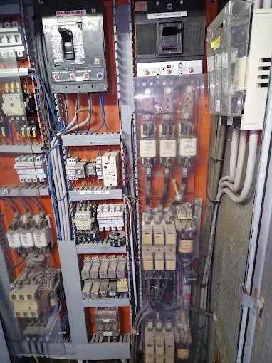 Una persona utilizza un cacciavite per lavorare su apparecchiature elettriche in un'officina, con fili e componenti ben visibili.