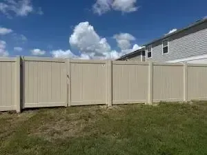 Beige vinyl fence beside a grassy yard under a blue sky with clouds