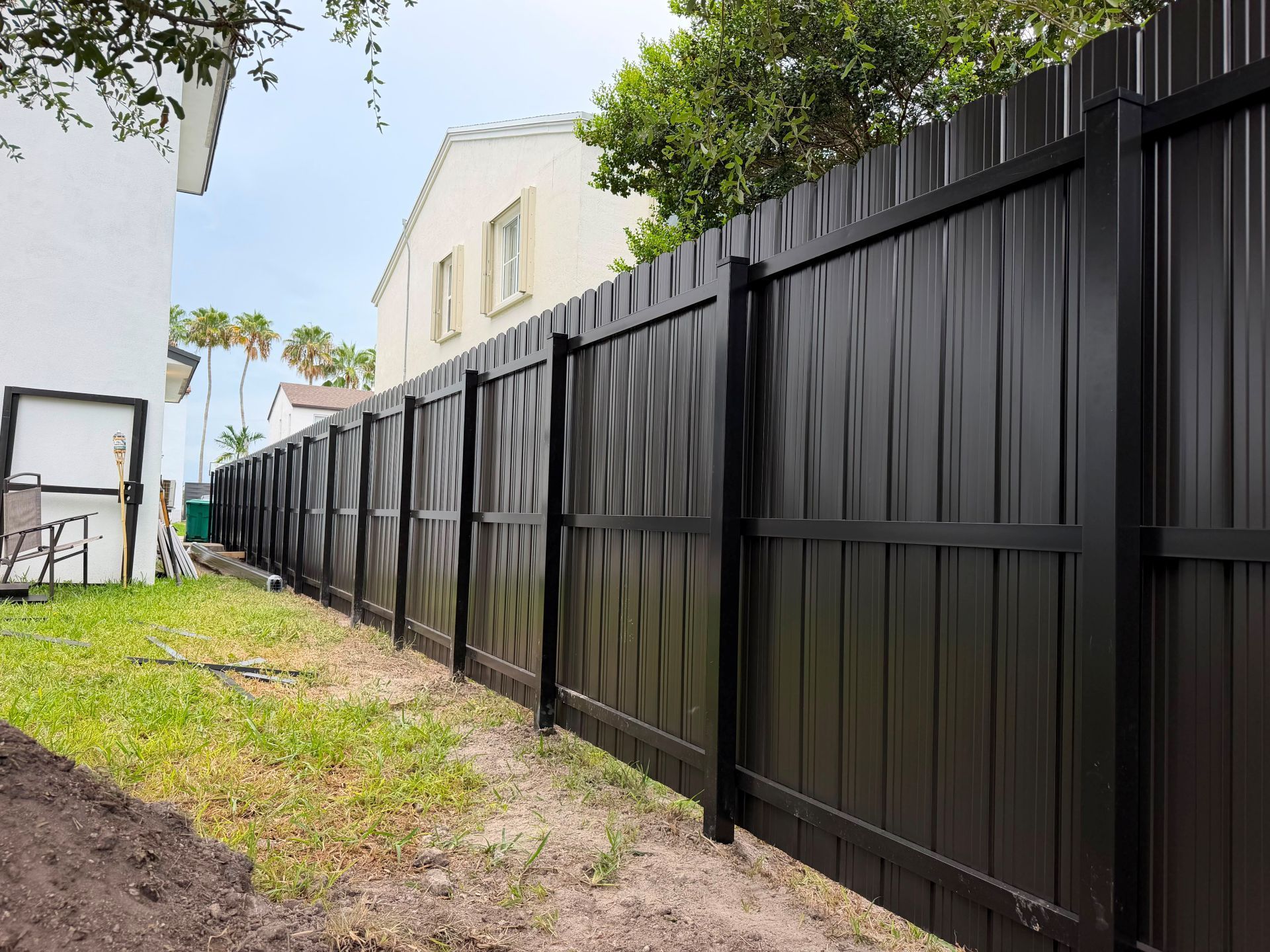 Long black metal fence along a narrow yard beside white houses under trees