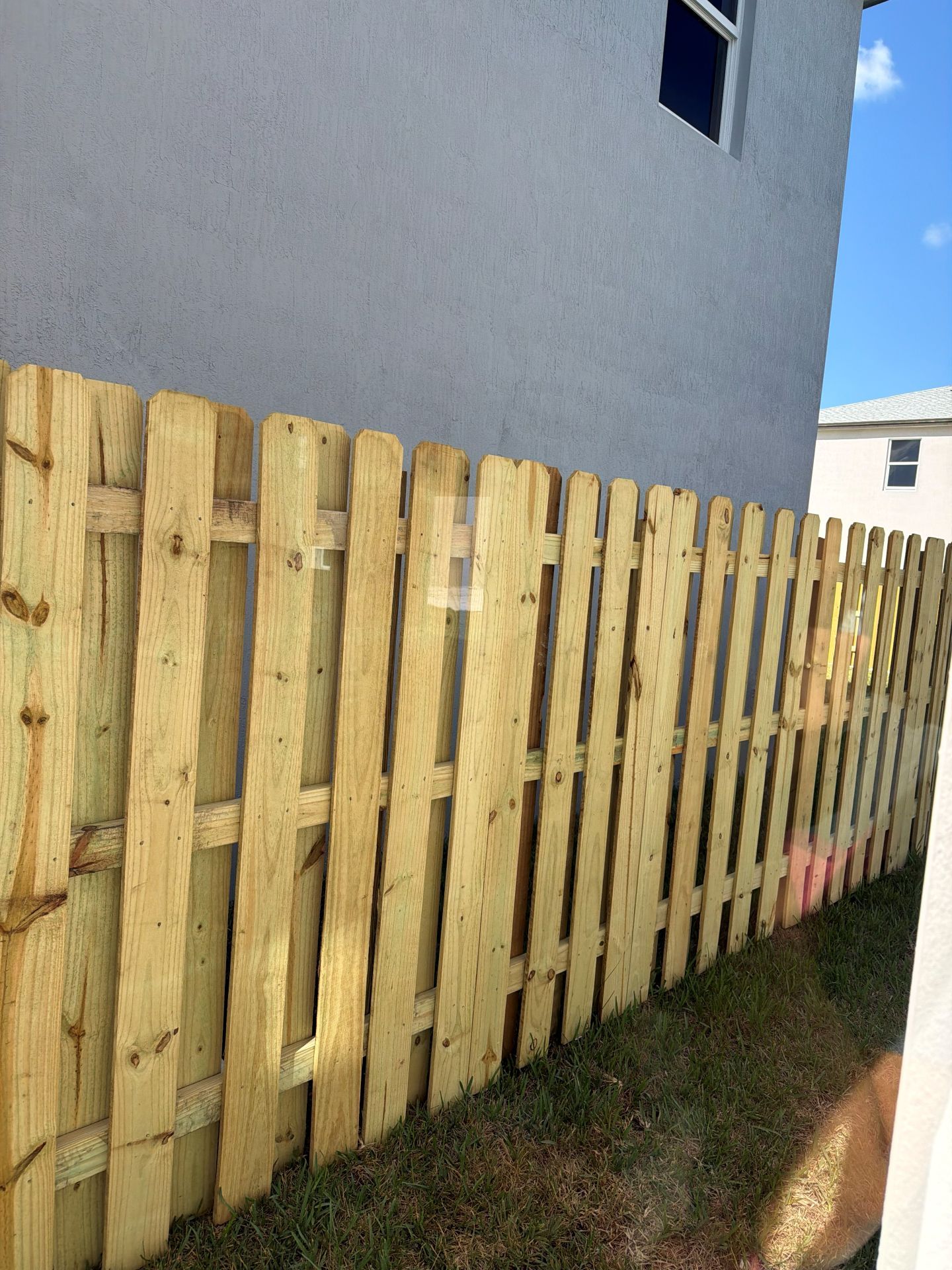 Wooden slat fence beside a gray house, lining a narrow grassy side yard