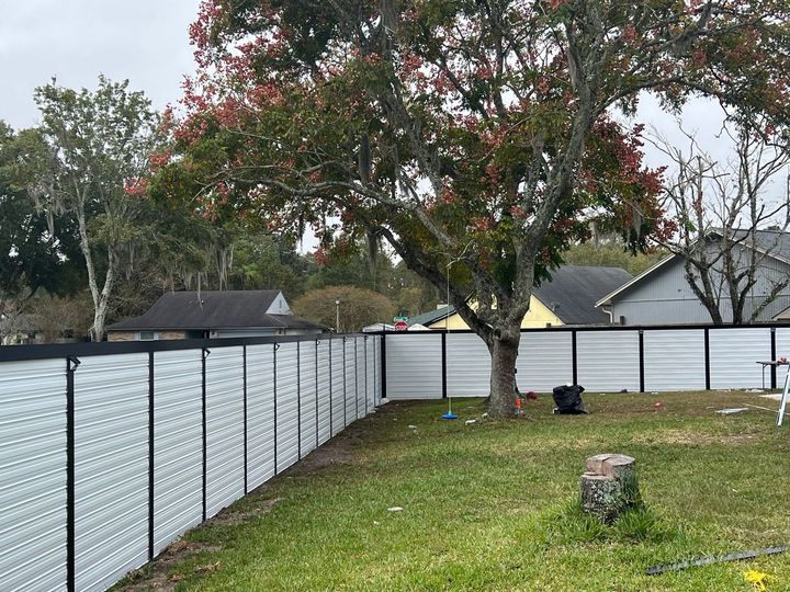 Backyard with a long white fence, a large tree, and a tree stump on the grass.