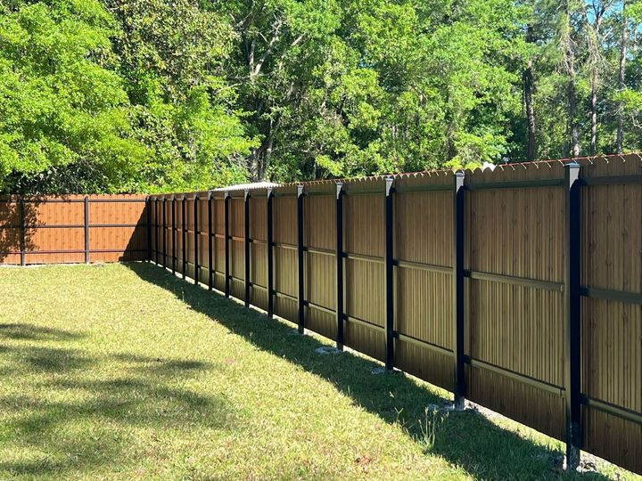 Long wooden fence along a grassy yard beside green trees in bright sunlight