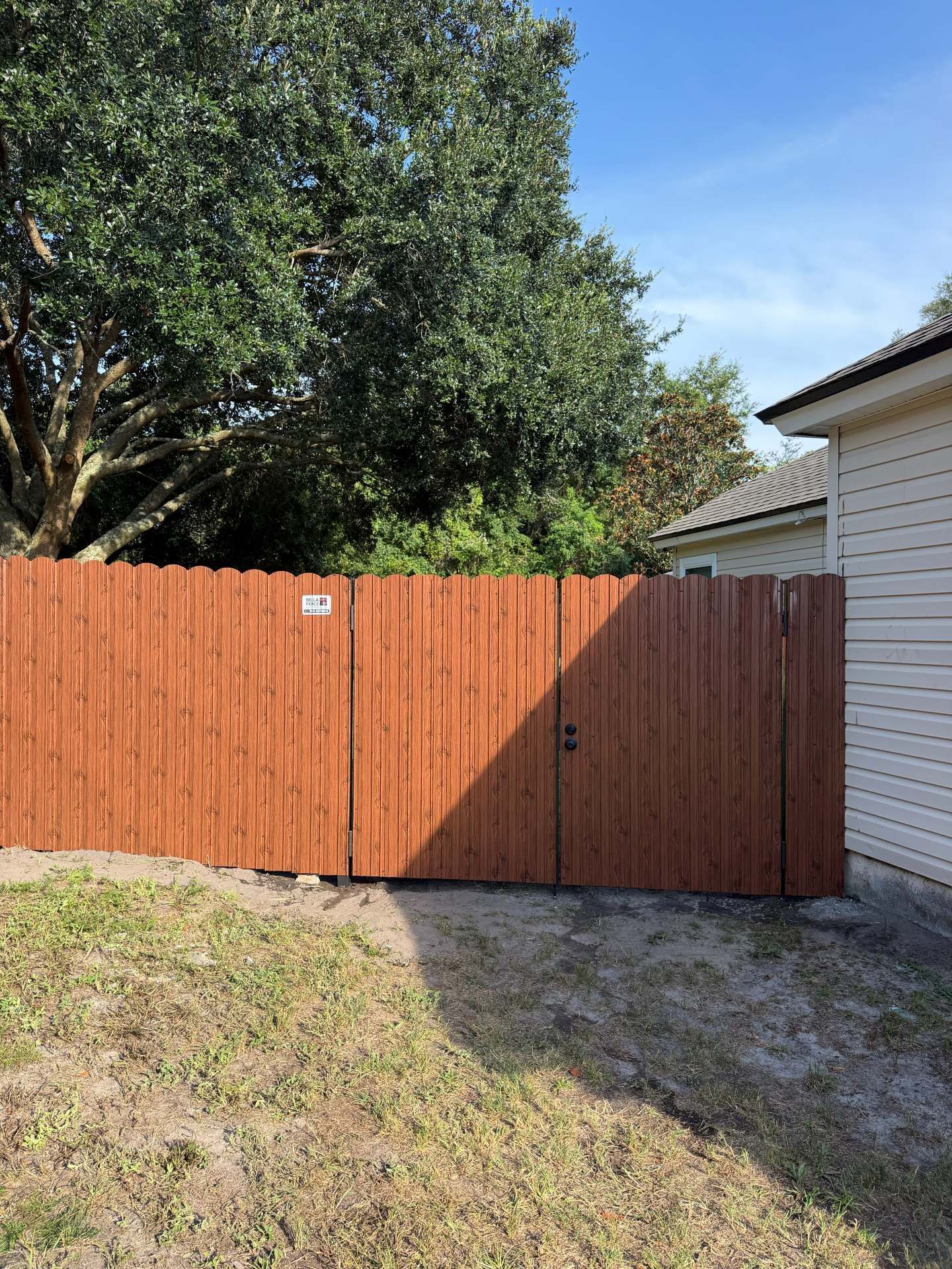 Orange wooden fence across a grassy yard beside a house, with a large tree behind it.