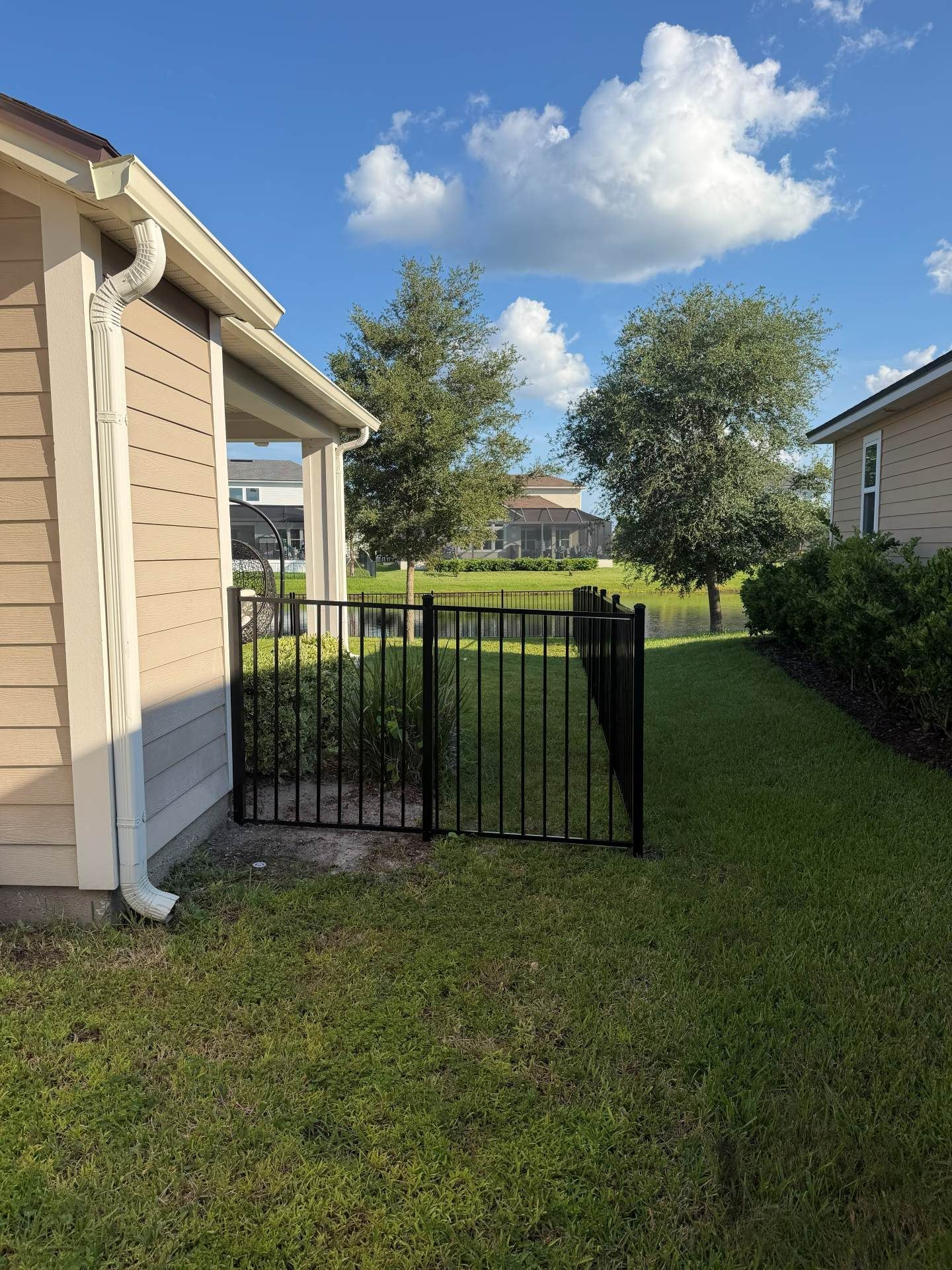 Backyard gate between beige house and hedge under a bright blue sky