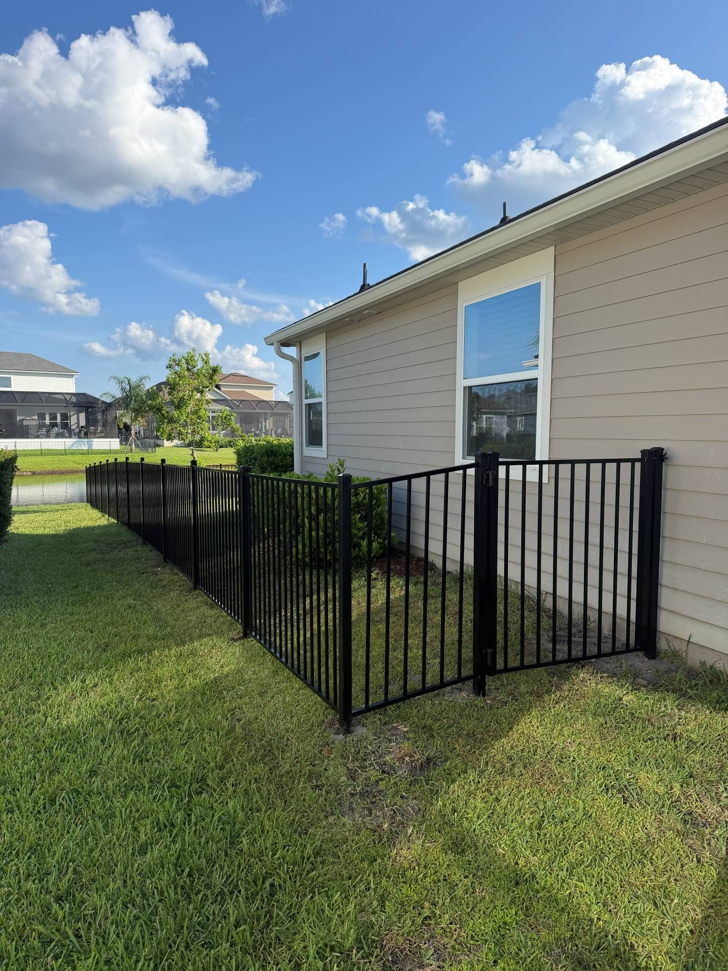 Black metal fence enclosing a side yard beside a beige house under a blue sky
