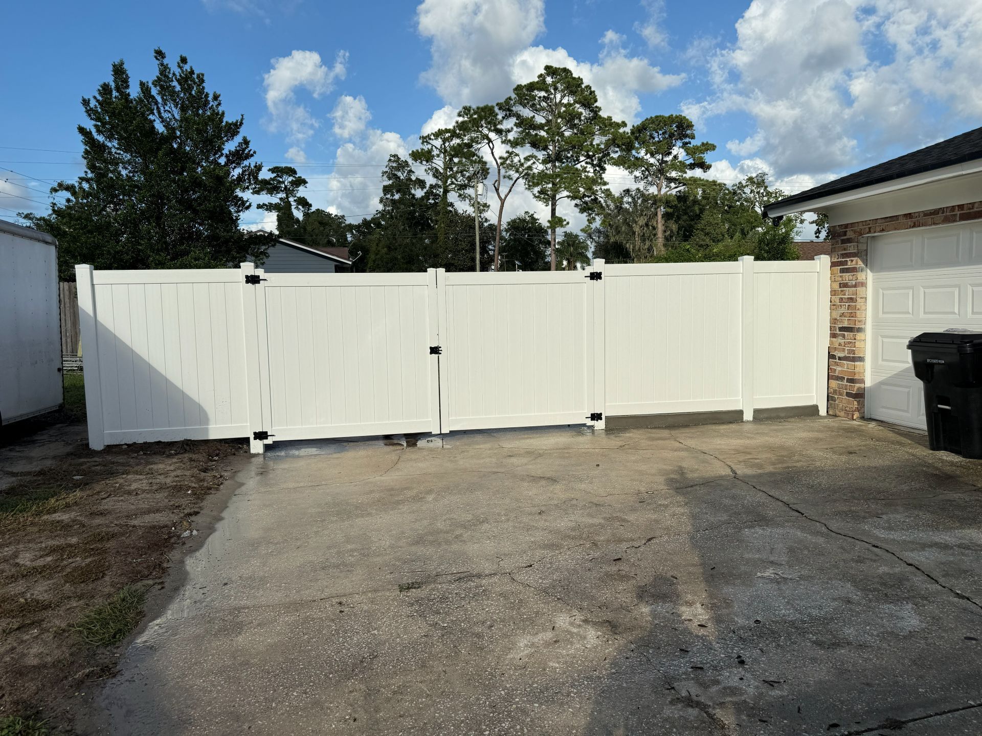 White privacy fence across a concrete driveway beside a house under a blue sky