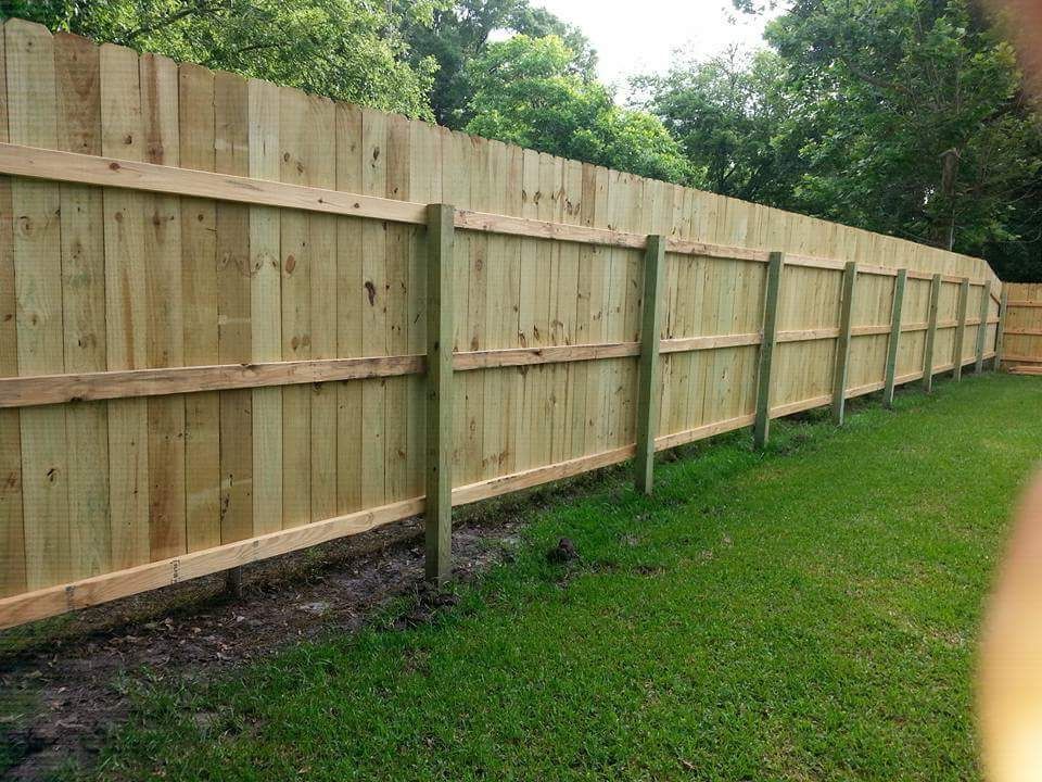 Wooden privacy fence running along a grassy yard beside trees