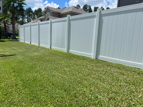 White vinyl fence along a green lawn with trees and houses in the background