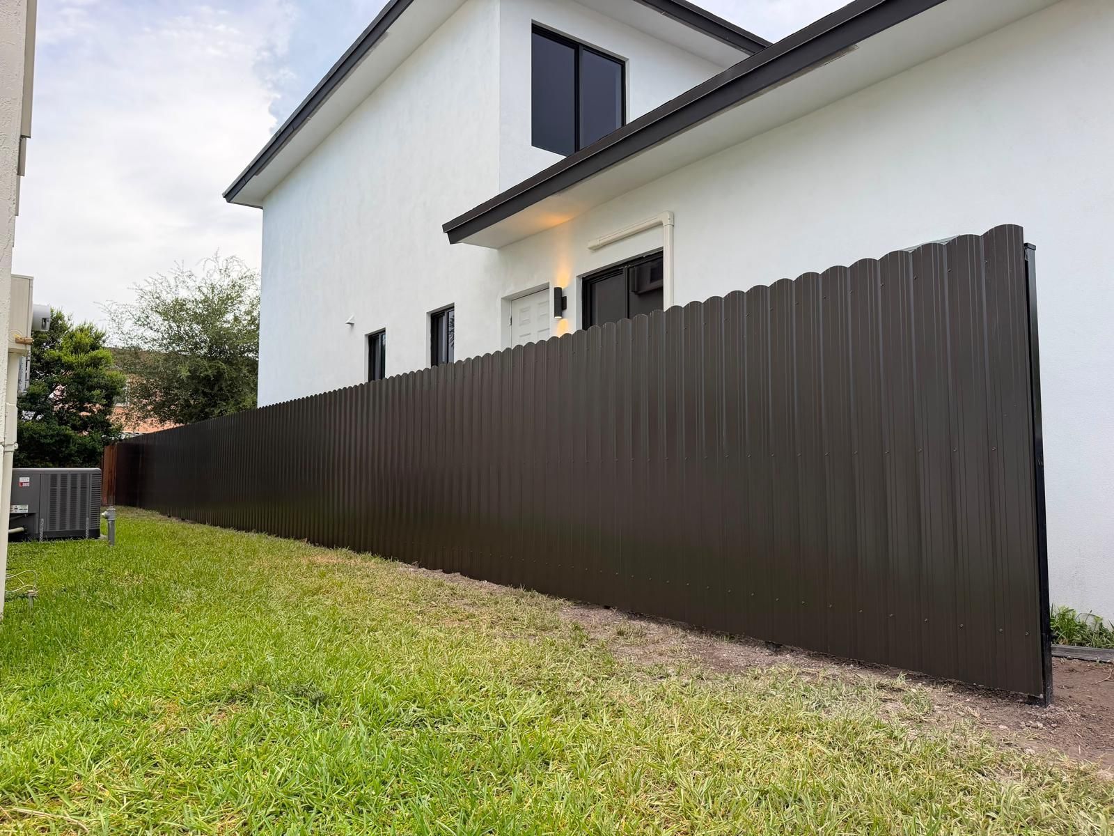 White two-story house with a dark fence along a grassy yard under a cloudy sky