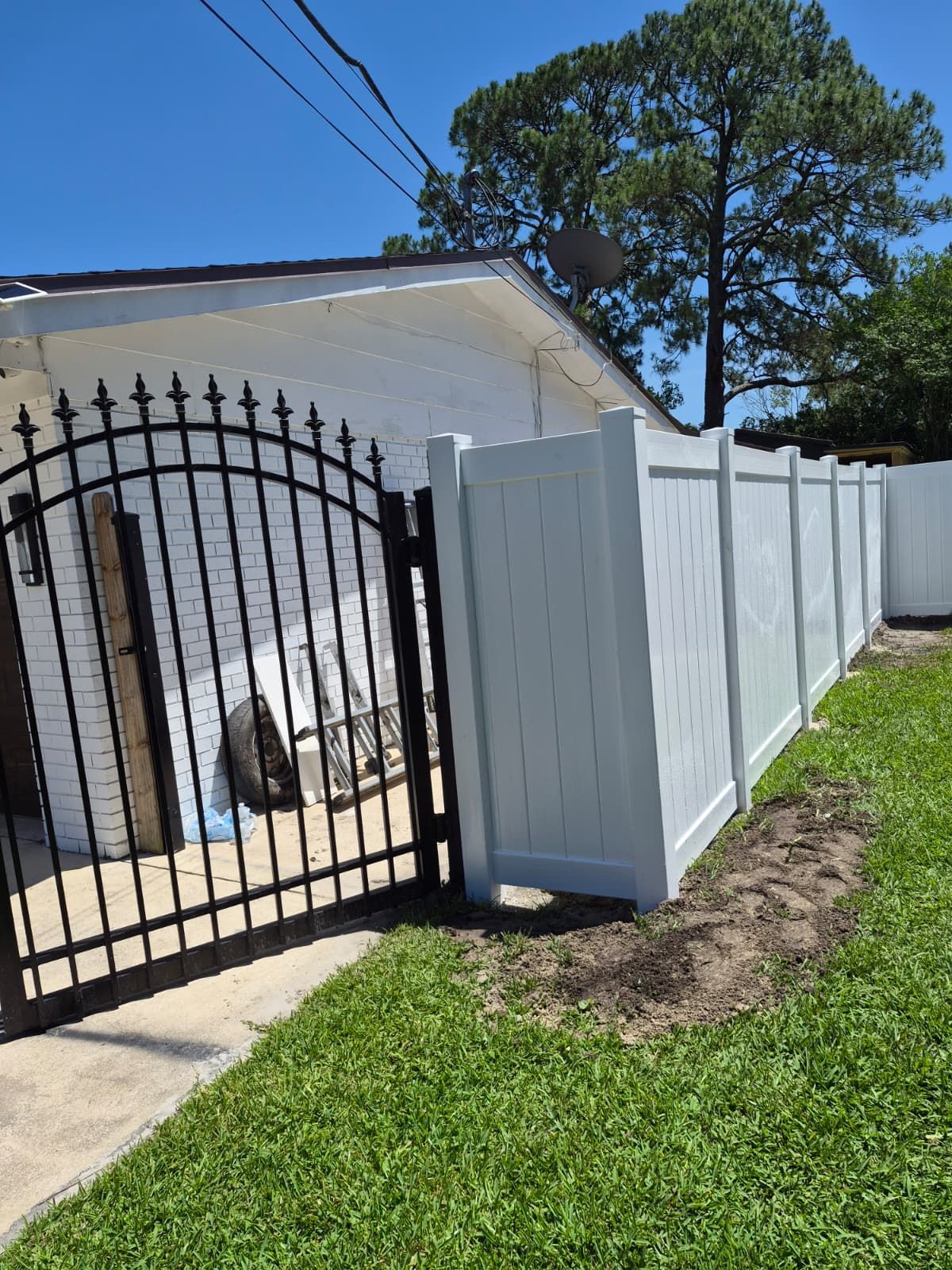 Black wrought-iron gate beside a white privacy fence along a sunny residential sidewalk