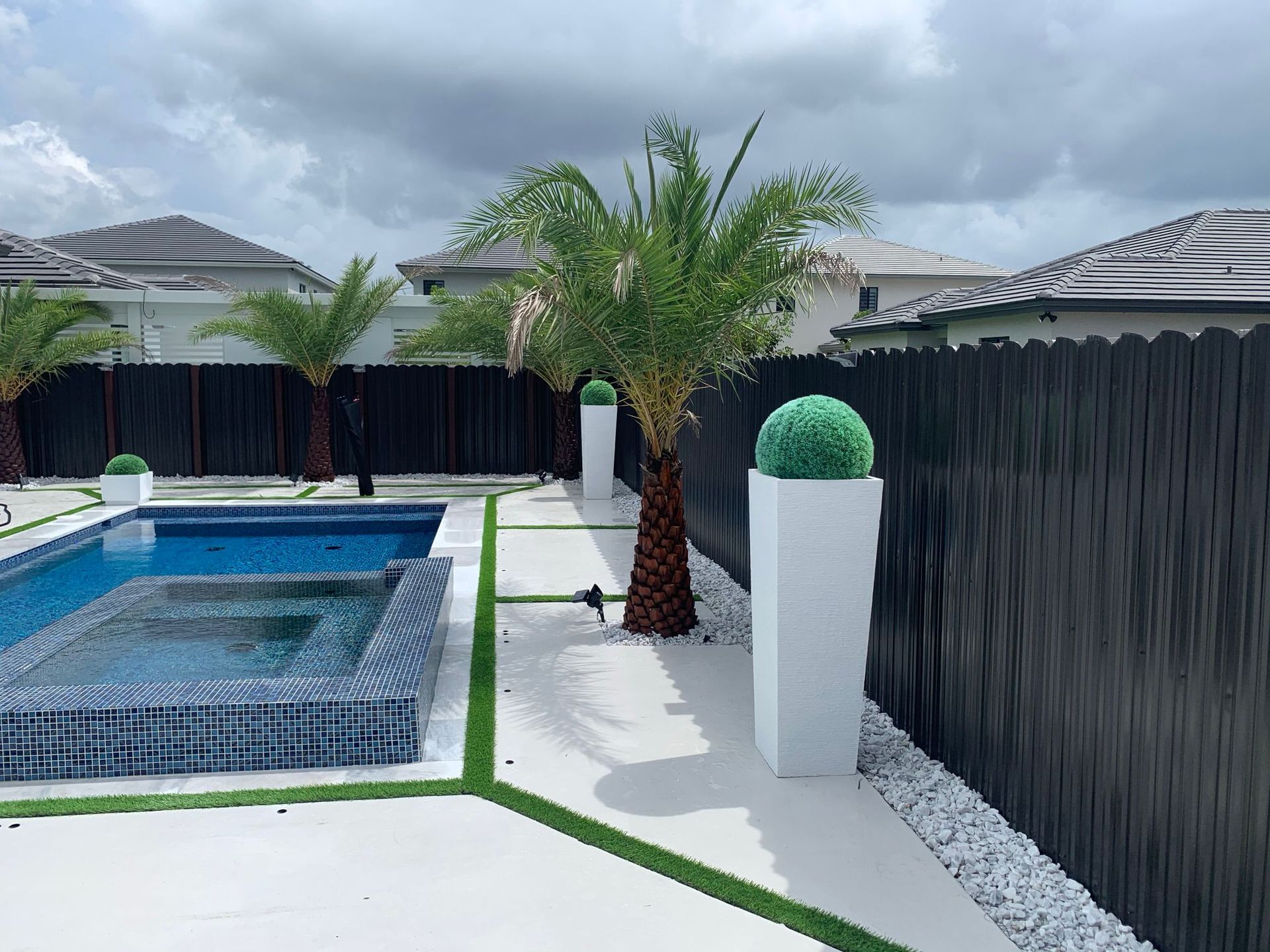 Backyard pool with palm trees, black privacy fence, and white gravel landscaping