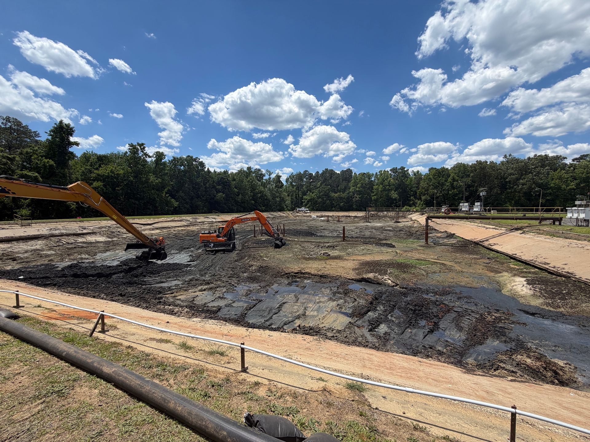 Two excavators clearing sludge from a dewatered aeration basin with treatment plant catwalks and railing visible in North Carolina