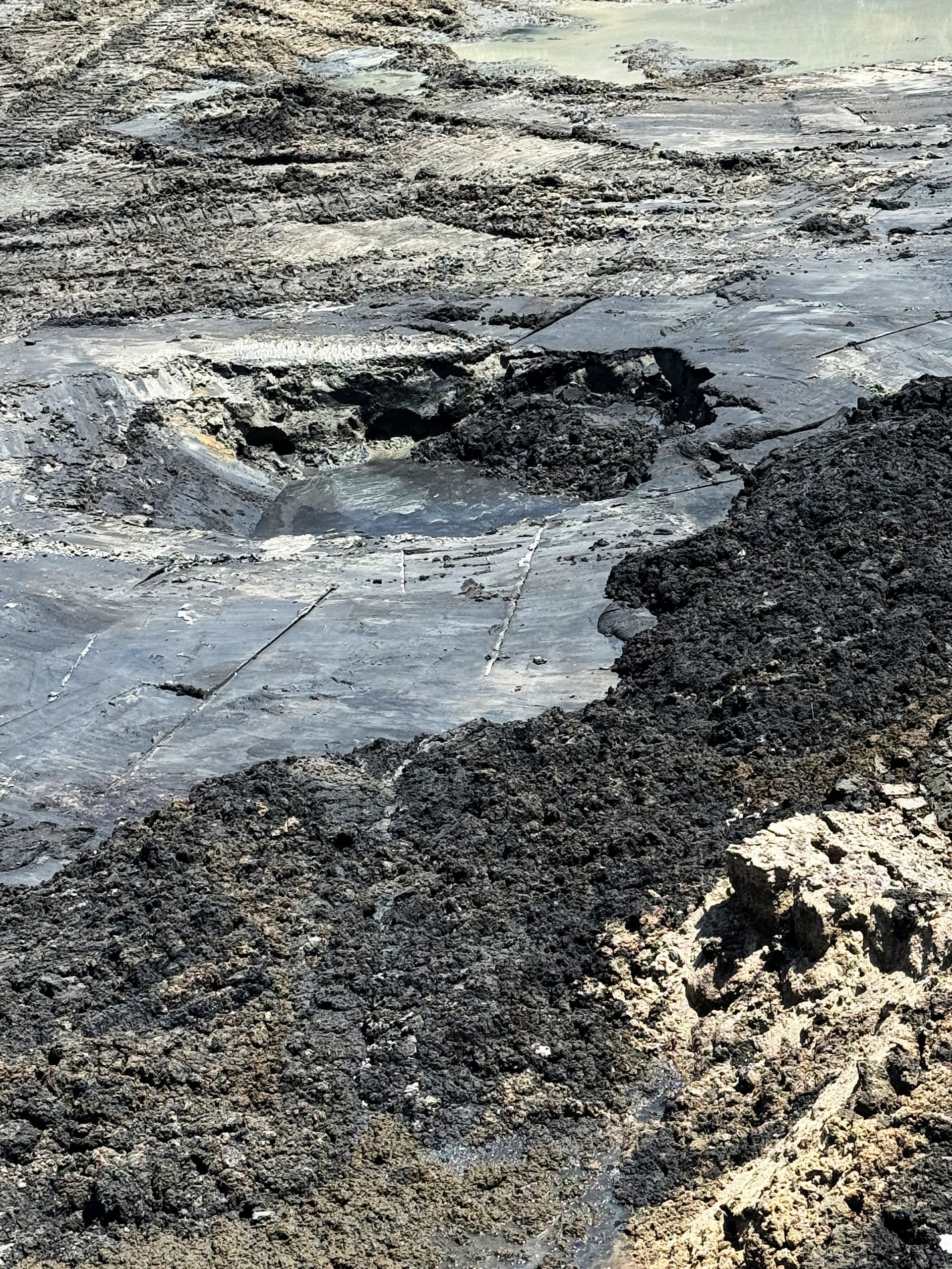 Close-up of deep sludge with standing water pockets inside a dewatered aeration basin before solidification in North Carolina
