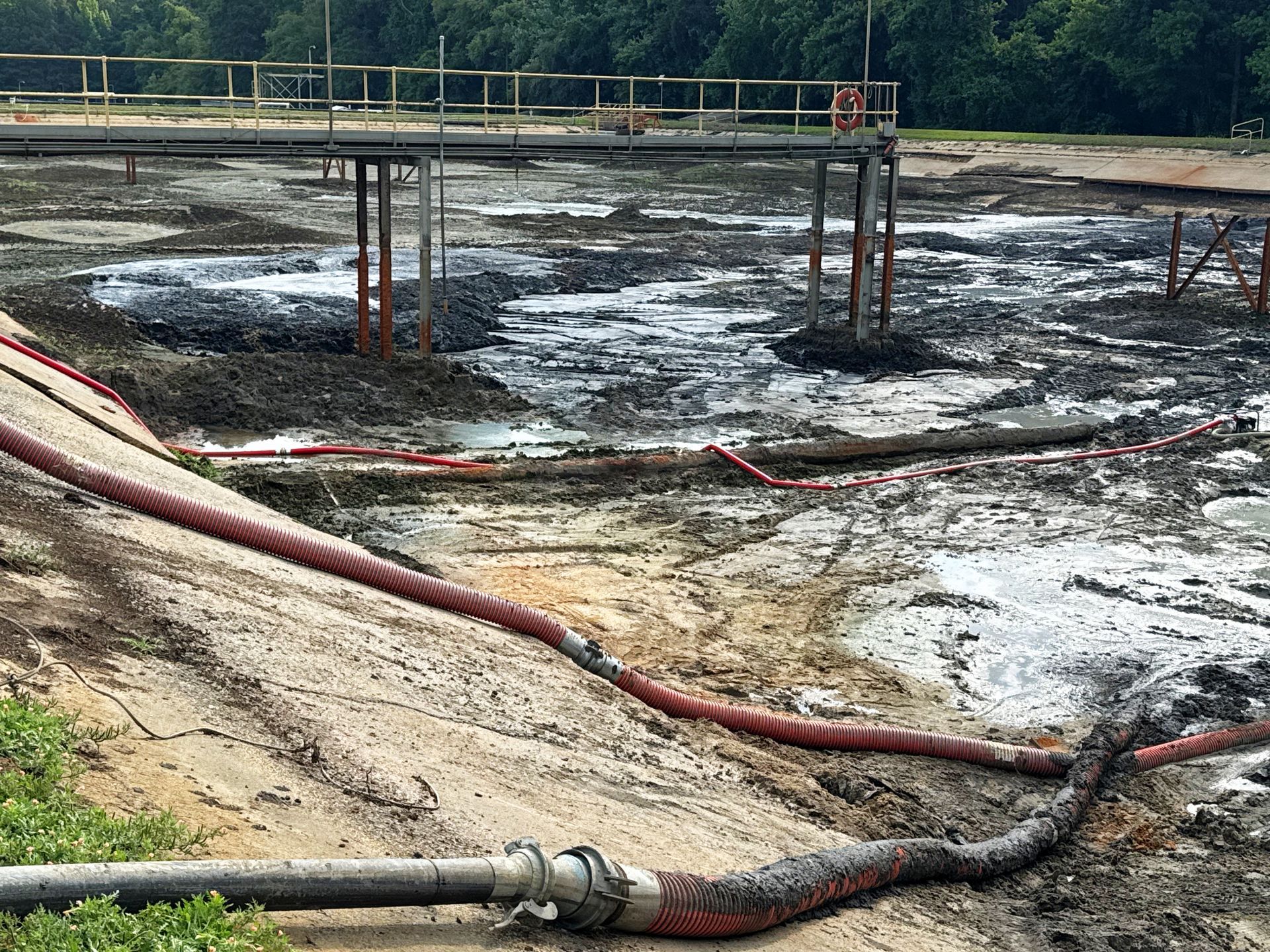 Dewatering hoses running into a partially drained aeration basin with catwalk and life ring visible during North Carolina lagoon cleanout