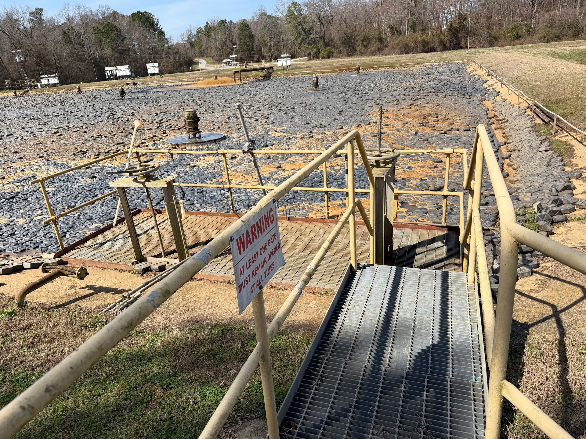 Catwalk with warning sign overlooking aeration basin filled with hexagonal floating covers before sludge removal at a North Carolina wastewater facility