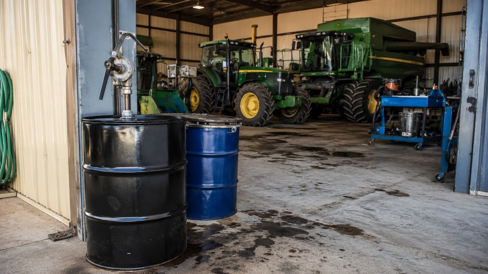 Used oil collection drums and hand pump staged beside farm equipment in an agricultural maintenance bay