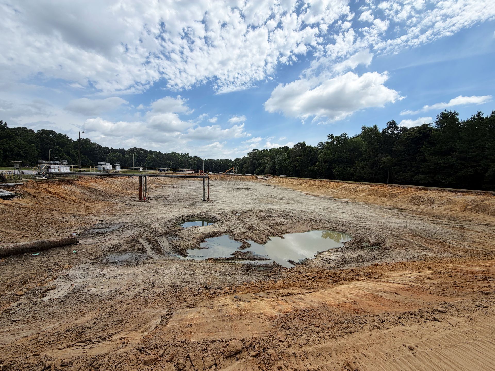 Cleared and regraded aeration basin with wastewater treatment plant infrastructure visible in the background in eastern North Carolina