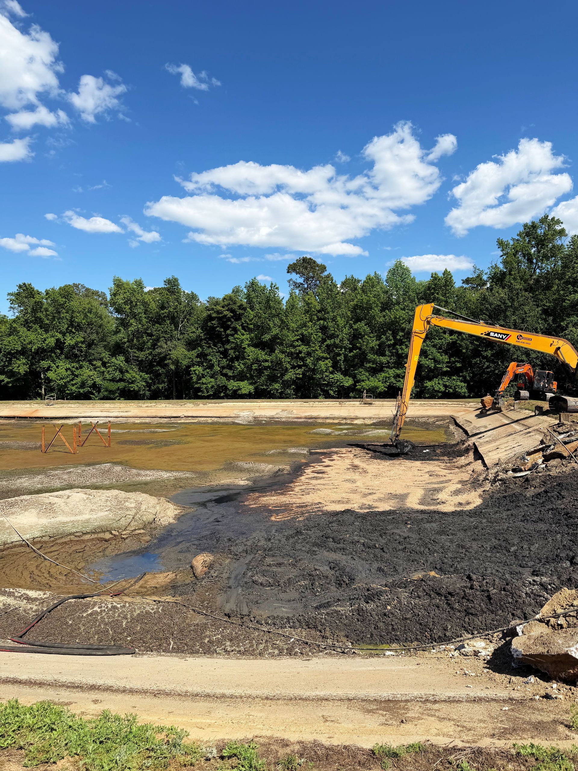 Long-reach excavator working remaining sludge alongside standing water during basin cleanout at a North Carolina wastewater facility
