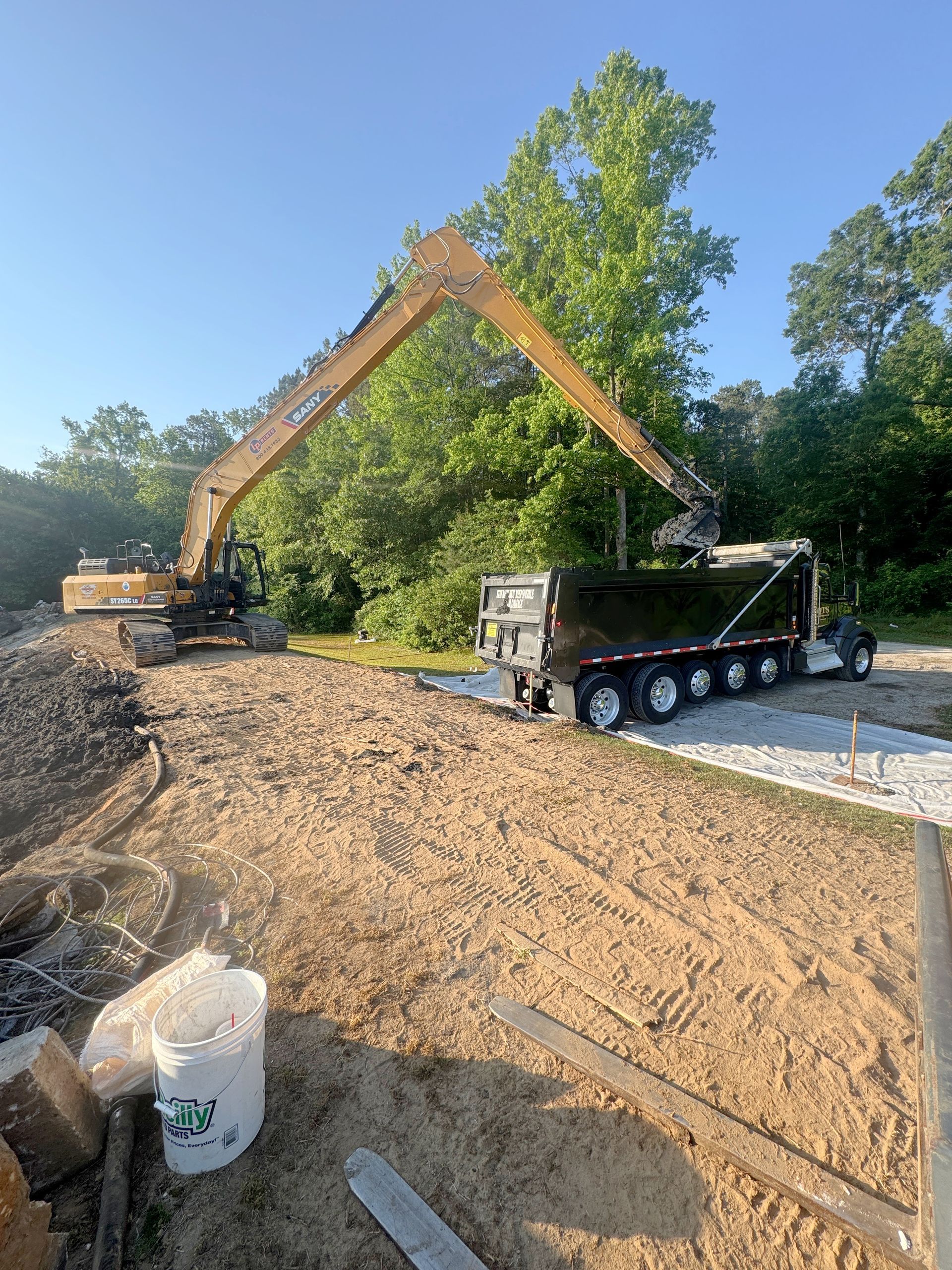 Long-reach excavator loading solidified basin sludge into a haul truck staged on geotextile during lagoon cleanout in North Carolina