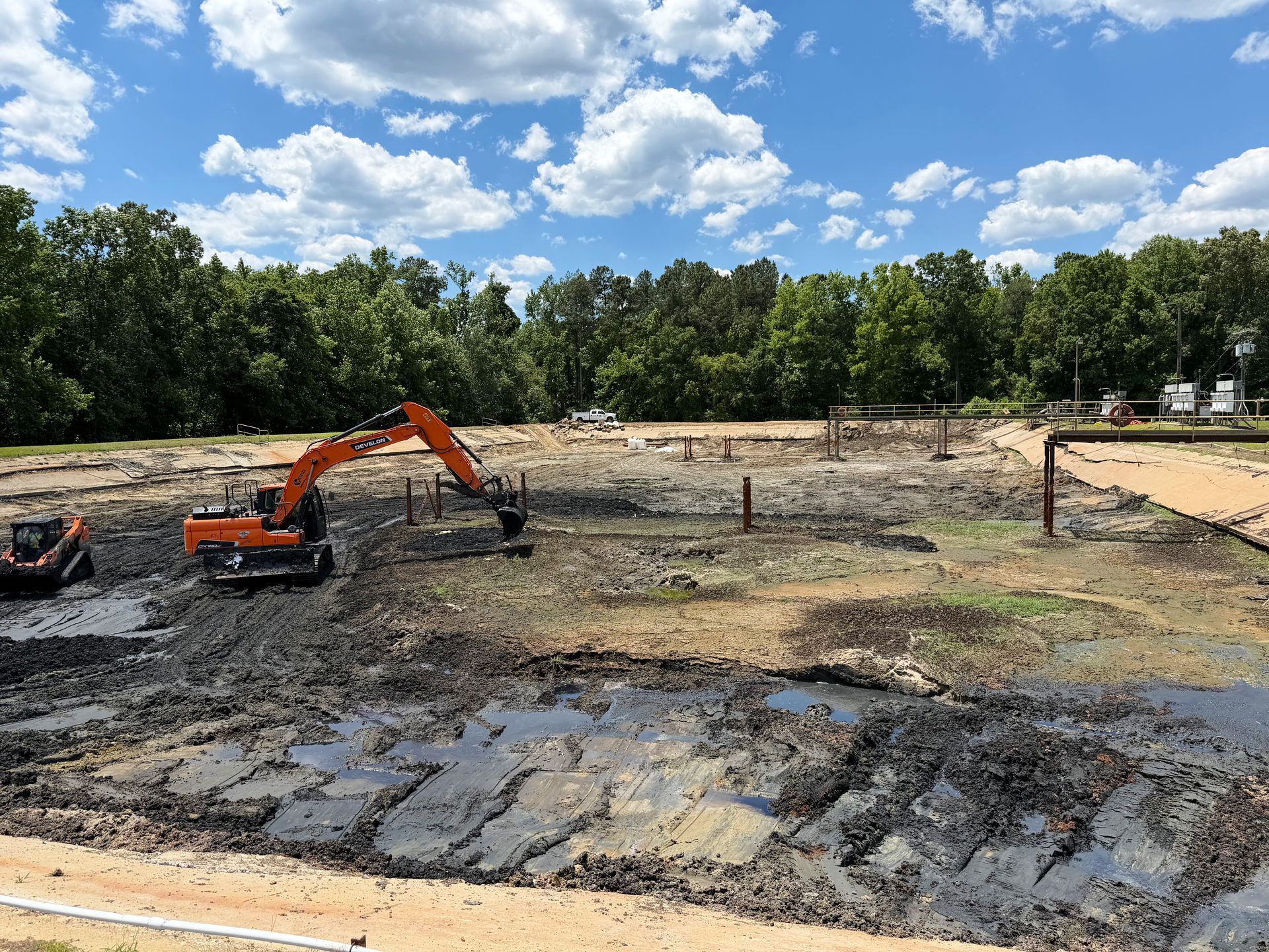 Tracked excavator and compact track loader clearing remaining sludge from an aeration basin with catwalks still standing in North Carolina