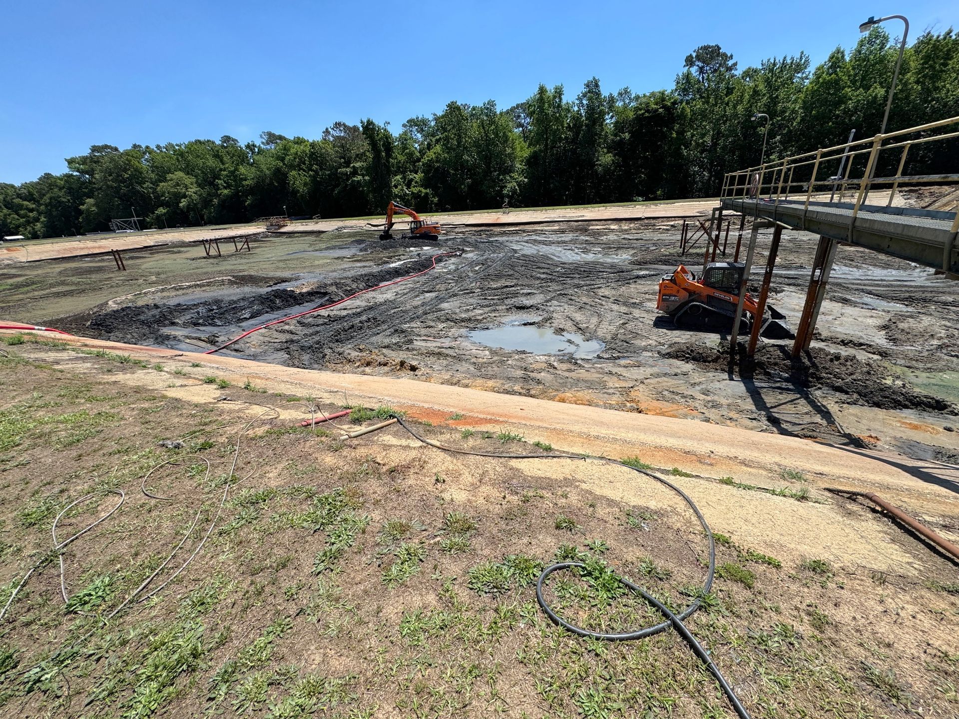 Compact track loader working near catwalk supports while excavator operates in the background during aeration basin cleanout in North Carolina