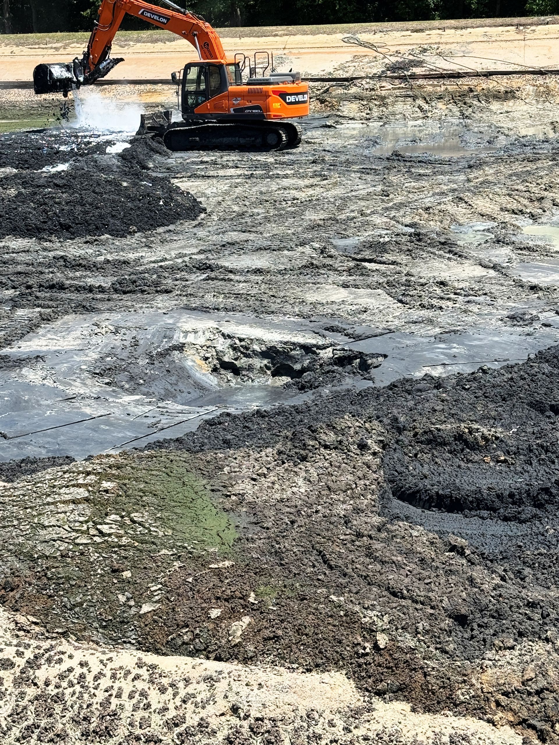 Tracked excavator working deep wet sludge during solidification and removal inside a wastewater aeration basin in North Carolina