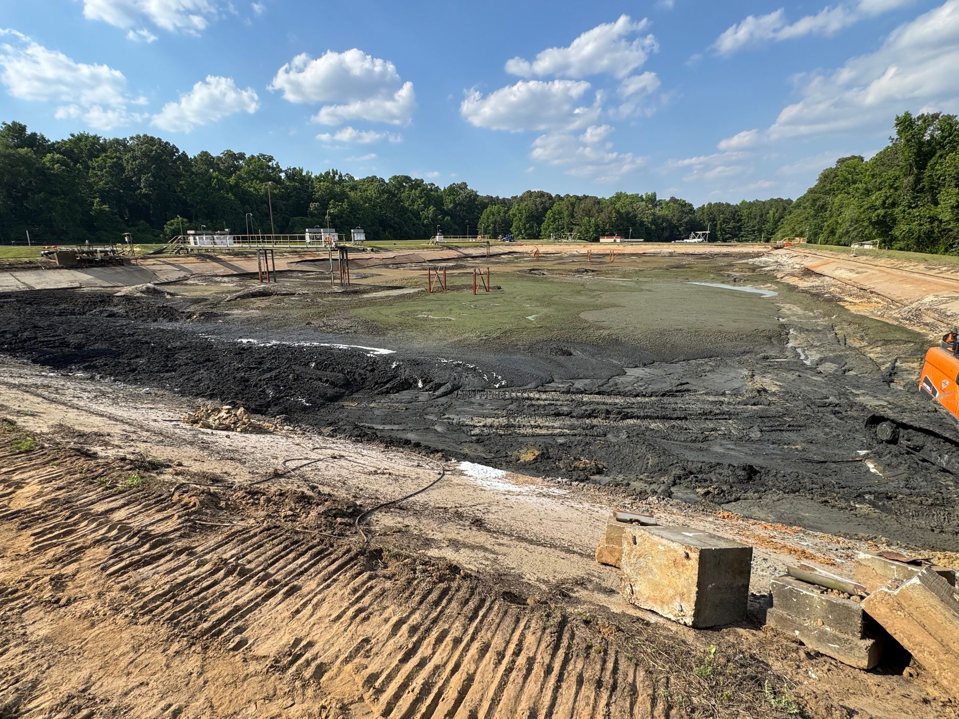 Mid-project view of aeration basin cleanout showing cleared sections alongside remaining sludge with wastewater plant infrastructure in North Carolina
