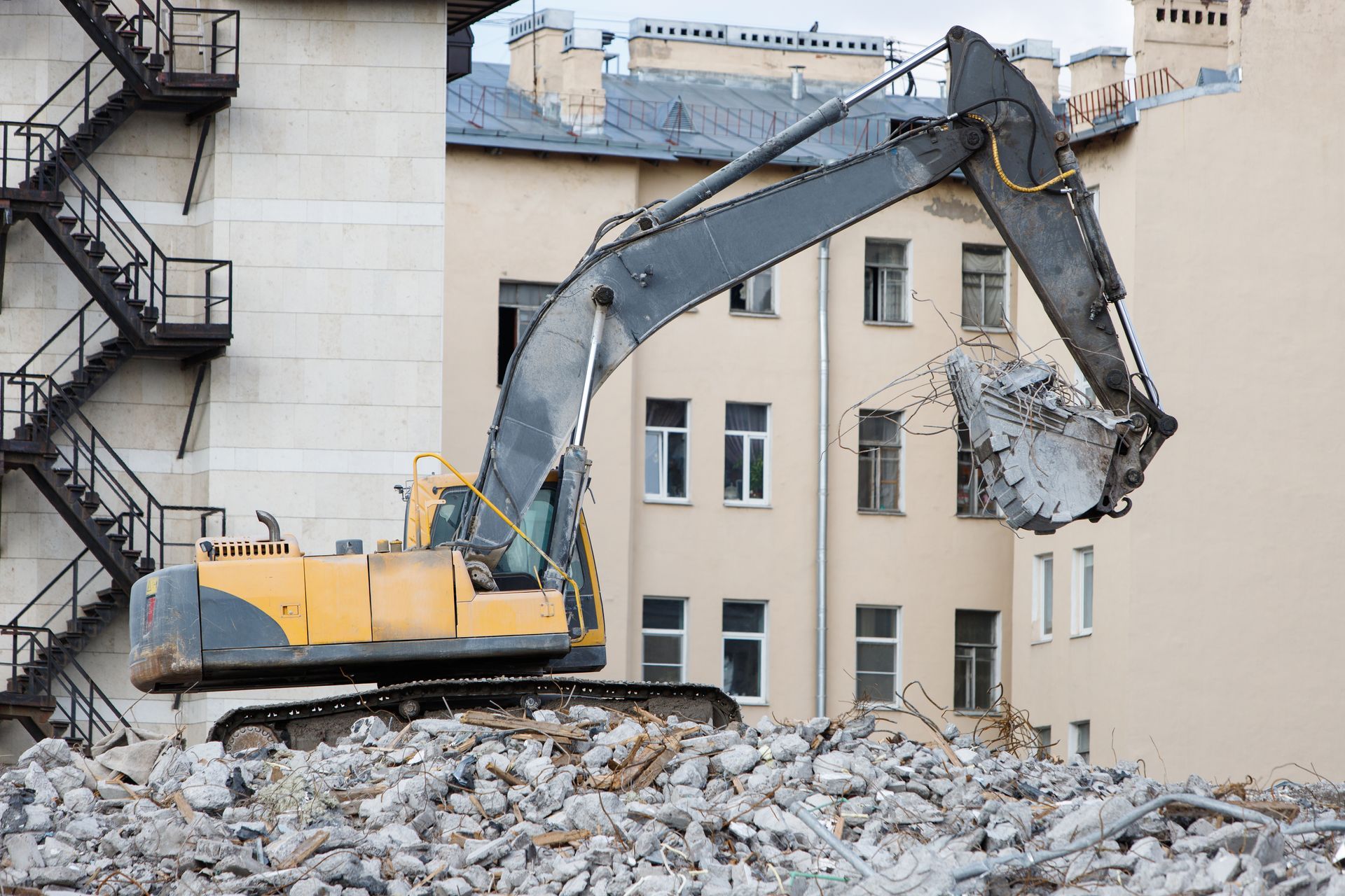 Excavator demolishing a building, with rubble piled in front of it.