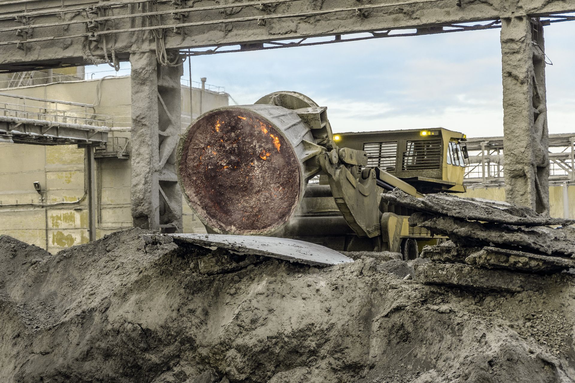 Heavy machinery pours glowing molten metal in an industrial foundry, with smoke and debris around it.
