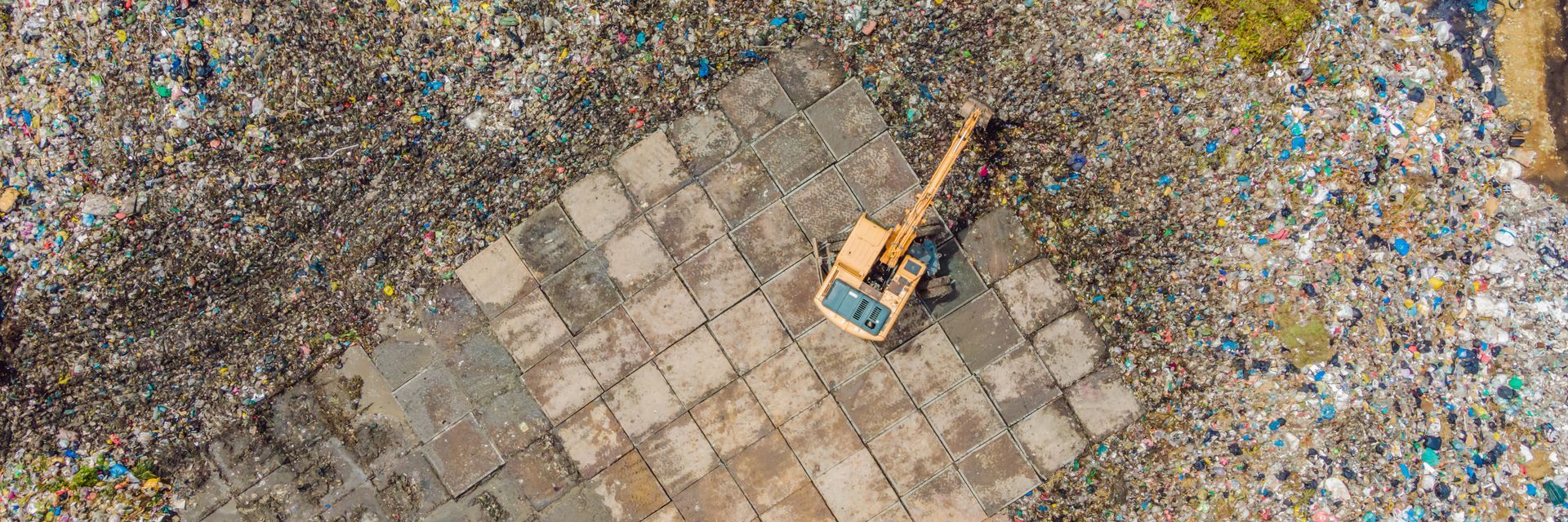 Excavator on a tiled patch amid a large heap of mixed debris and rubble