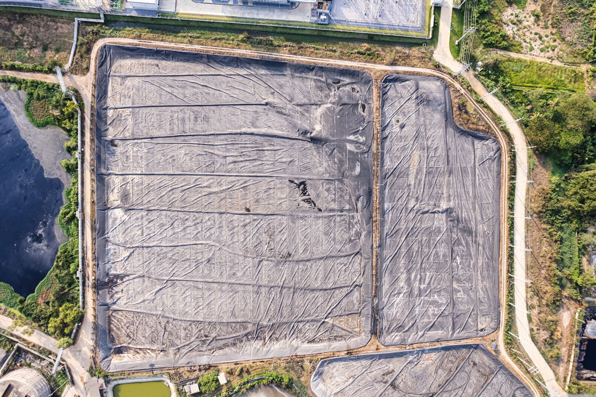 Aerial view of a large gray rectangular field bordered by dirt roads and vegetation