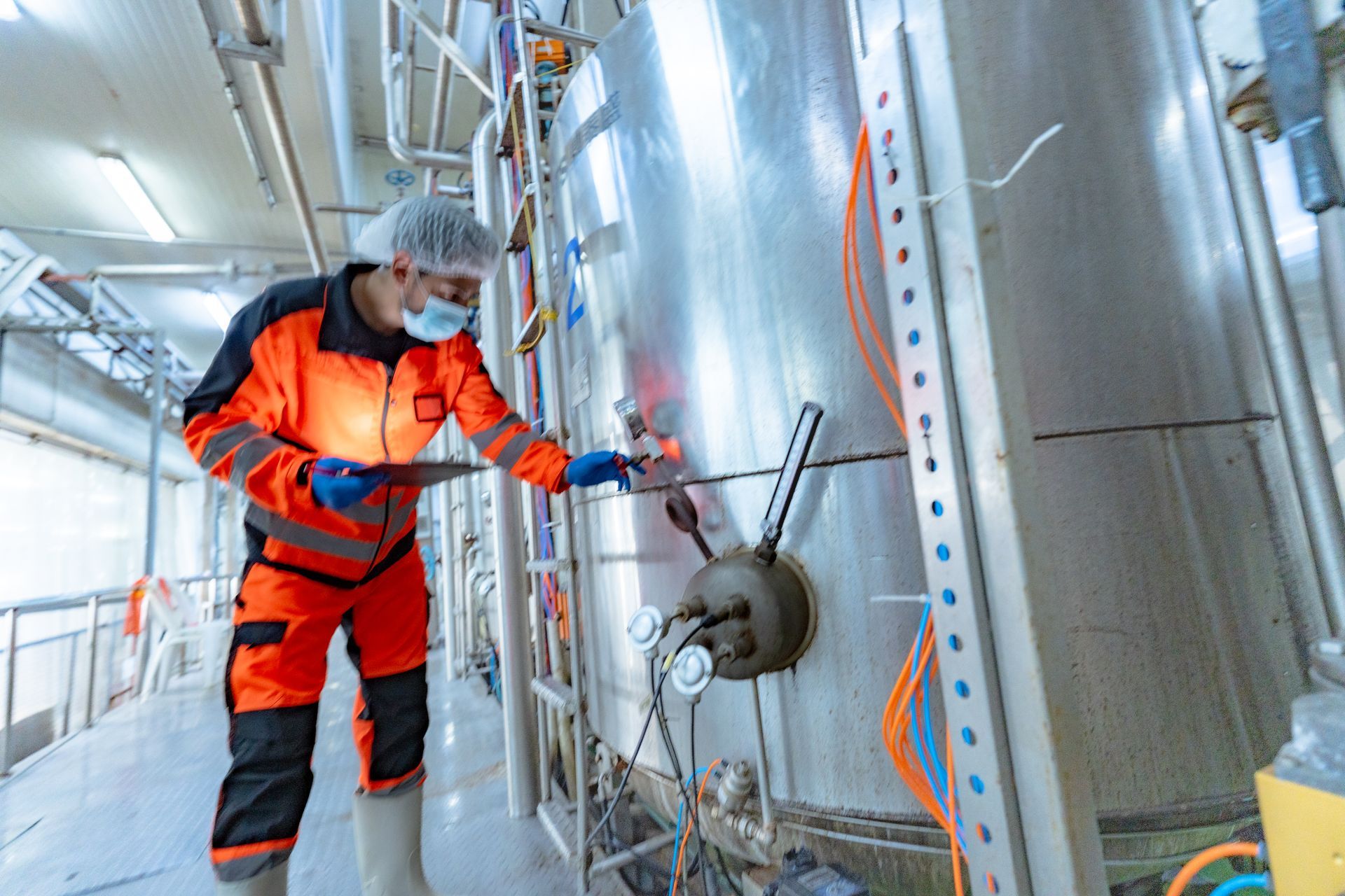 Industrial worker cleaning vessel interior using high-pressure equipment during chemical processing tank maintenance