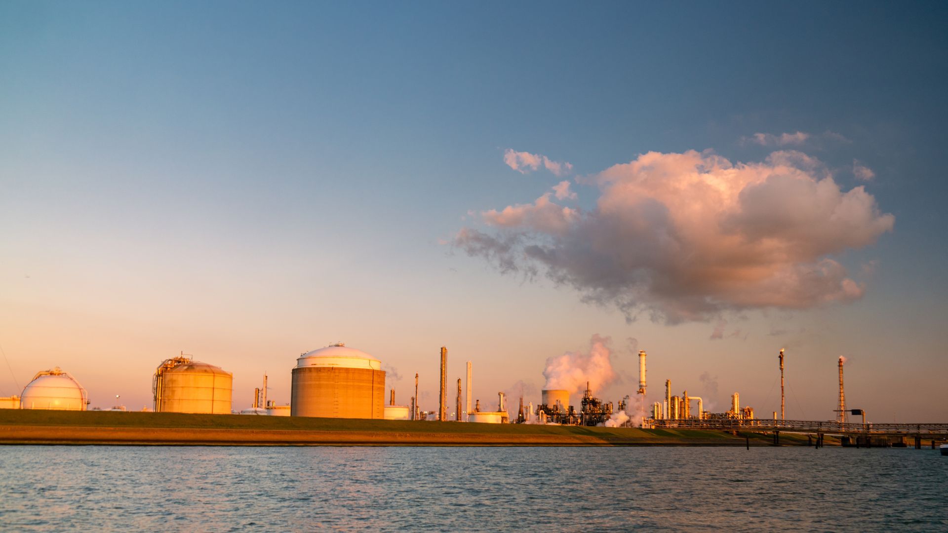 Large industrial plant with storage tanks and smoke stacks on shoreline
