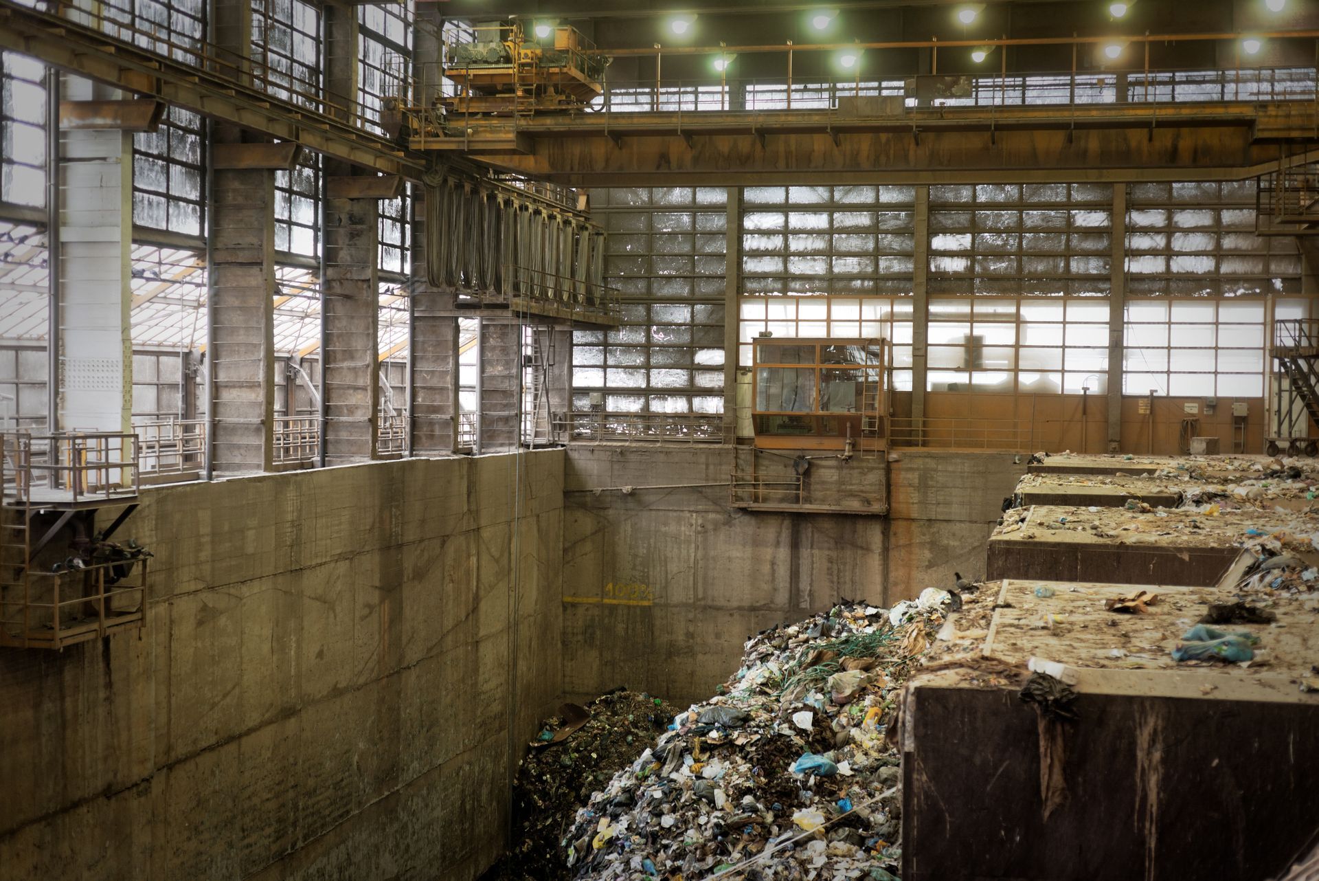 Abandoned industrial warehouse interior with a large concrete pit and piles of debris under tall windows