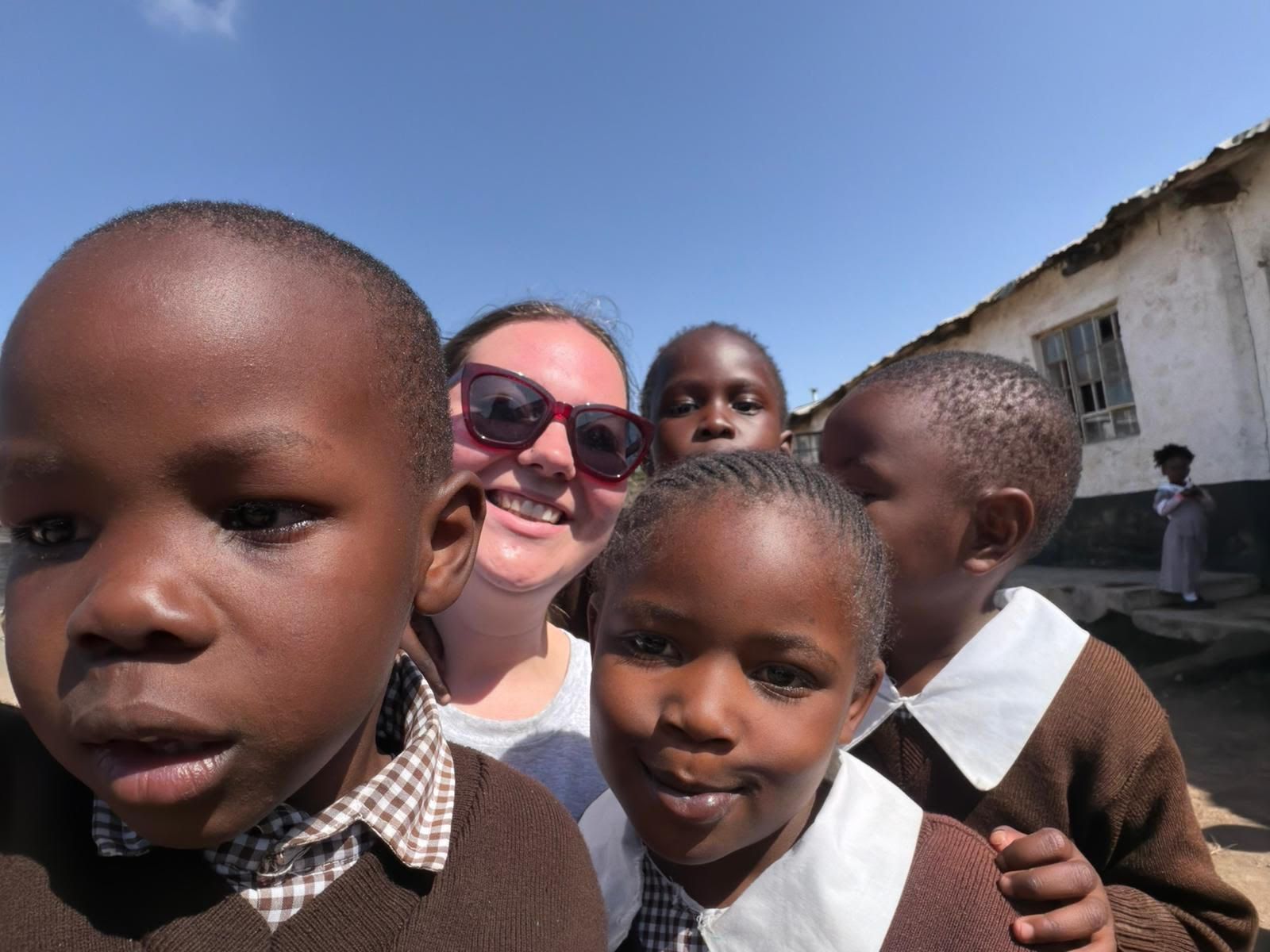 Children posing close to the camera with a smiling adult outdoors under a clear blue sky
