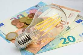 Una lampadina è posizionata sopra una pila di banconote e monete in euro.