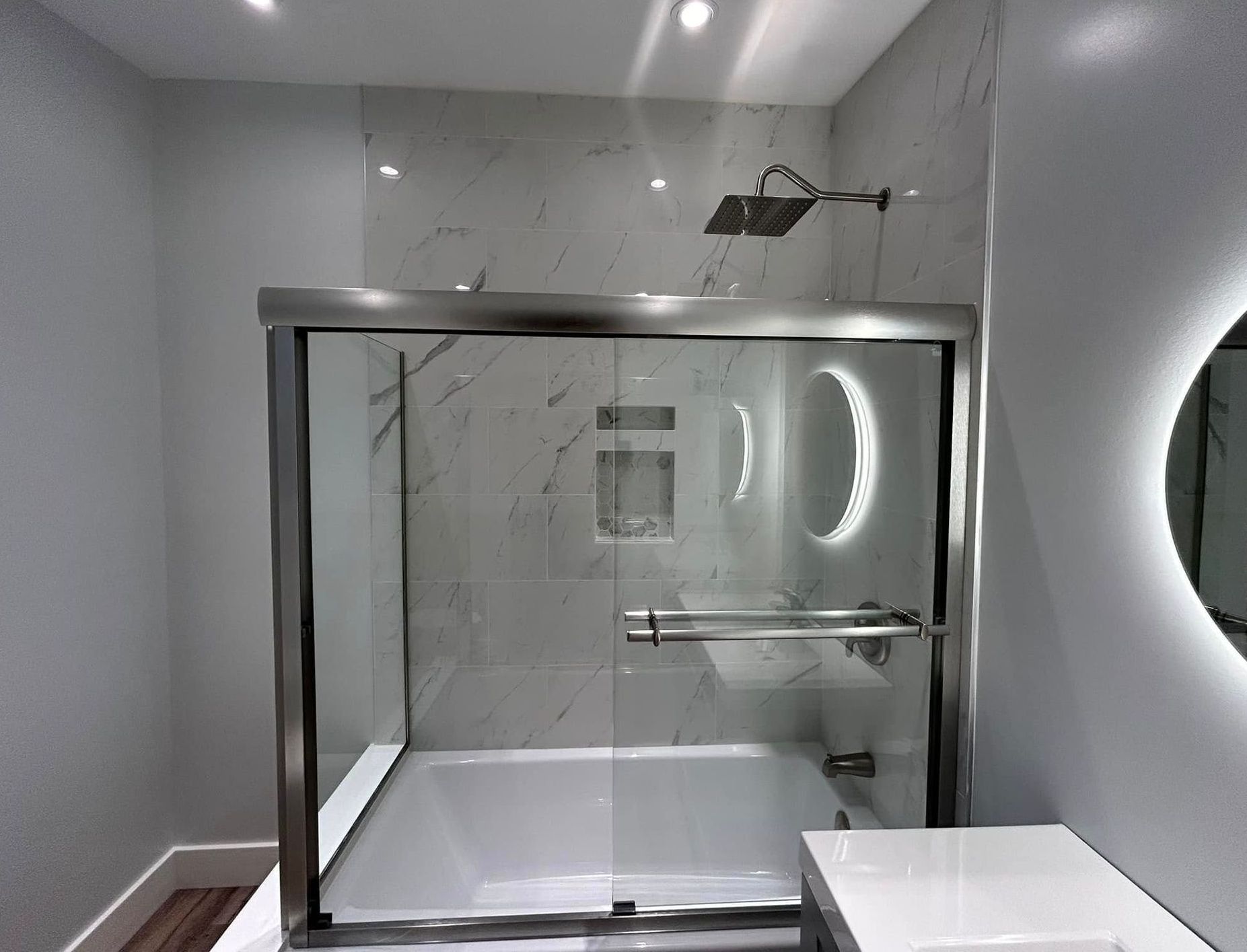 Bathroom with glass shower enclosure, marble tile, and a lit mirror.
