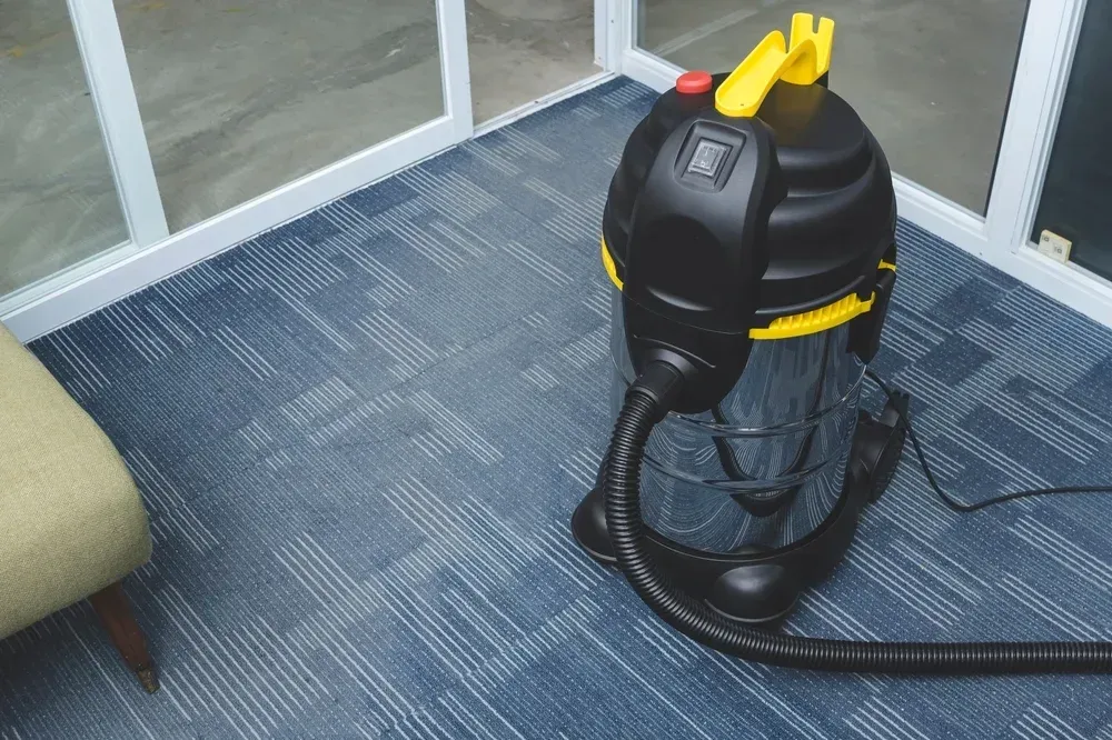 Black and yellow wet/dry vacuum on blue carpet beside a window and chair — Revive Cleaning & Restoration in Yeppoon, QLD