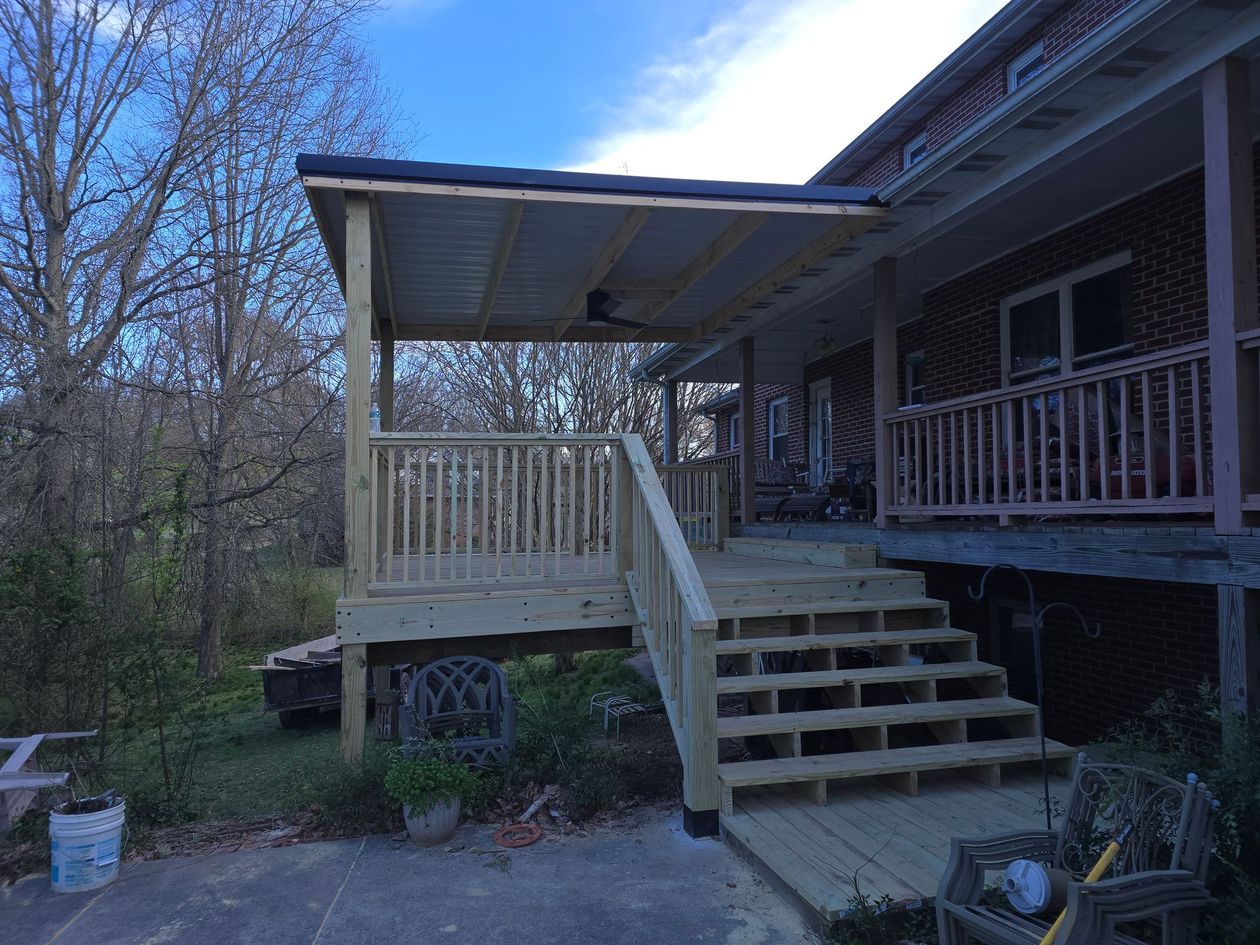 Front porch with wooden steps and railing on a house beside trees under a bright blue sky