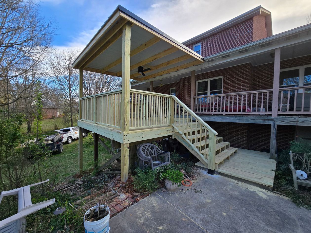 Yellow wooden porch and stairs attached to a brick house, with a driveway and yard below.