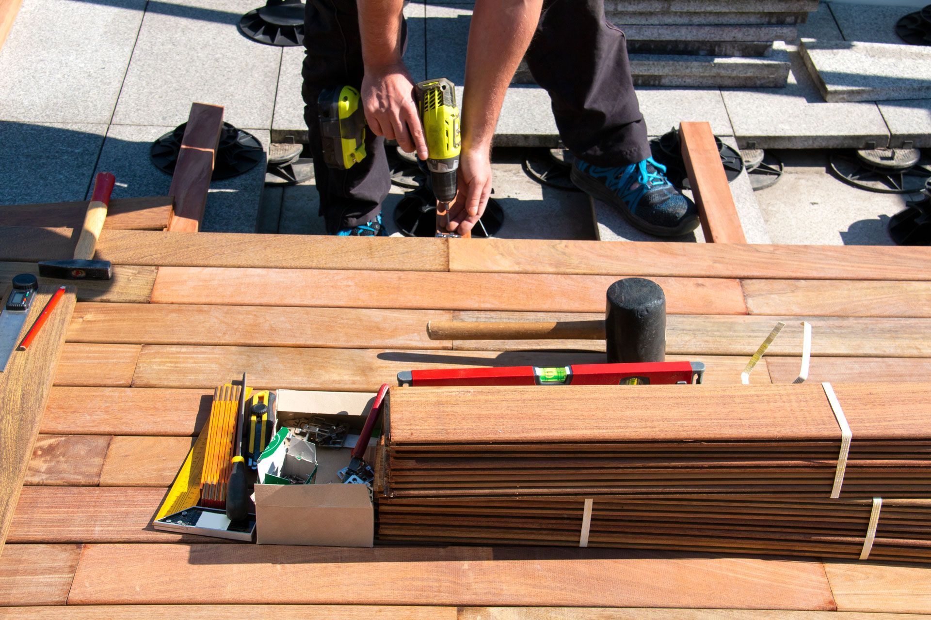 Person using a drill to install wooden deck boards. Tools and materials are nearby.